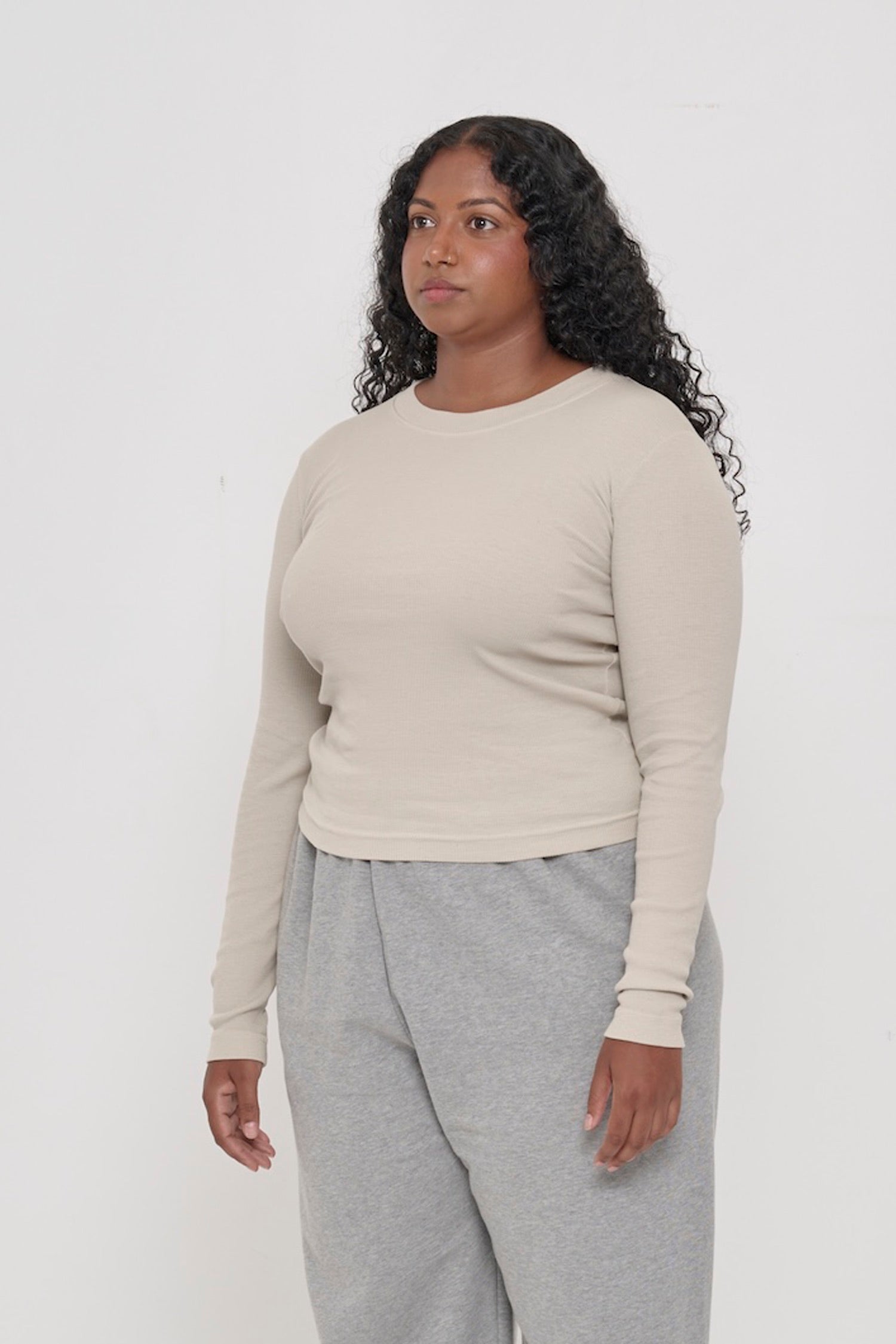 Woman turned 45-degrees from the front, in an Oat Rib Long Sleeve, shows side seams, heavy hem, and fitted silhouette.