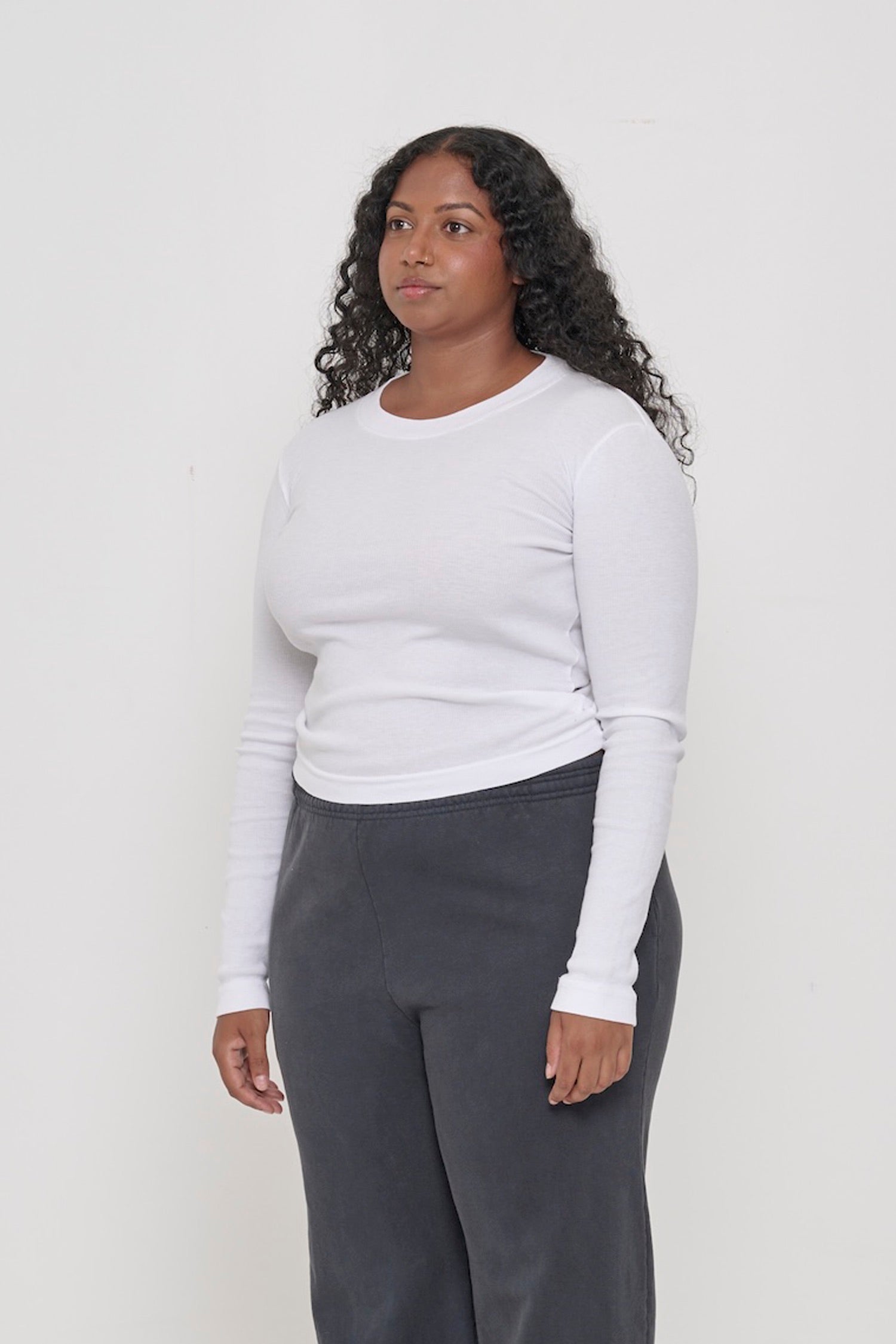 Woman facing 45-degrees from the front, in a White Rib Long Sleeve, Shows side seams, heavy hem, and fitted silhouette.