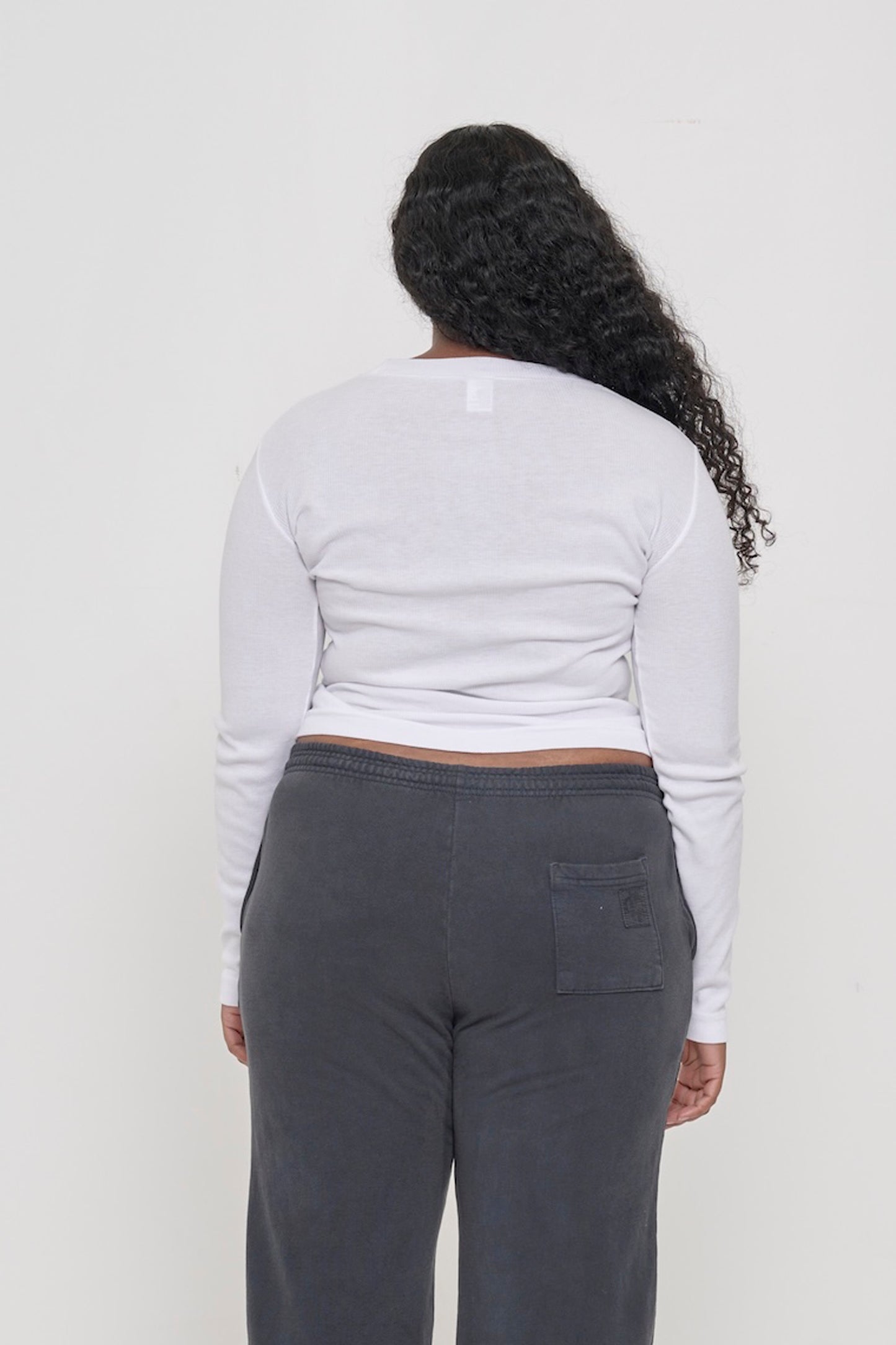 Back view: a woman in a White Rib Long Sleeve. Fitted across the upper back with a little ease across her mid to lower back.