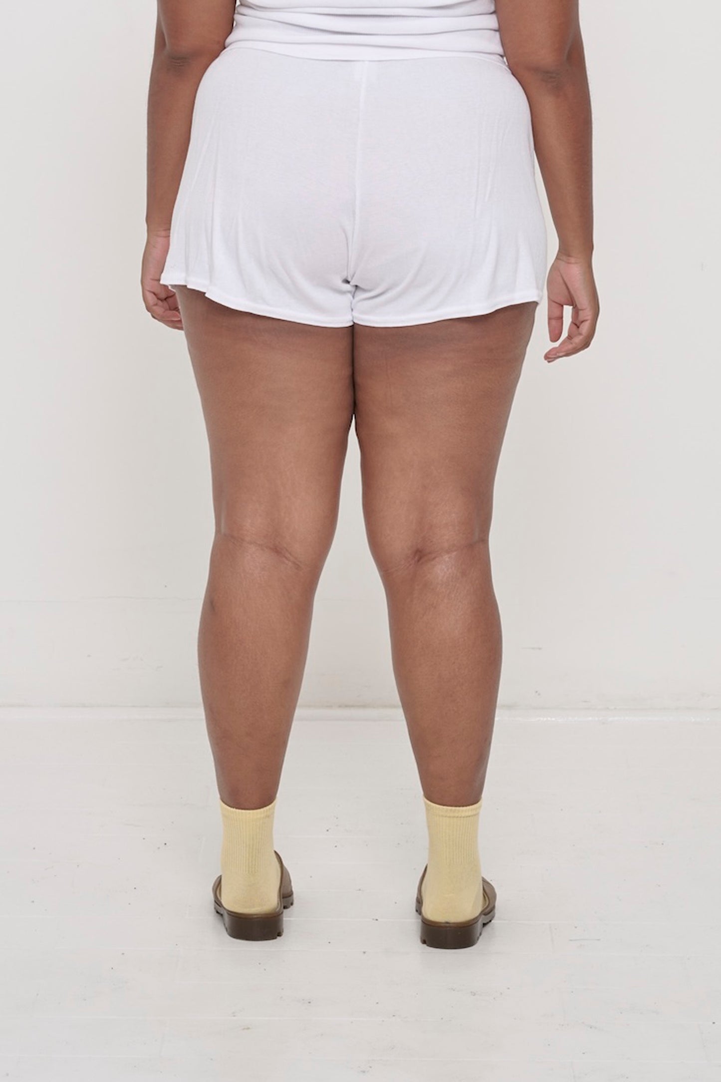 Back view: White Rib Shorts on a person, waist down. They feature a relaxed fit and a flowing, drapey fabric.