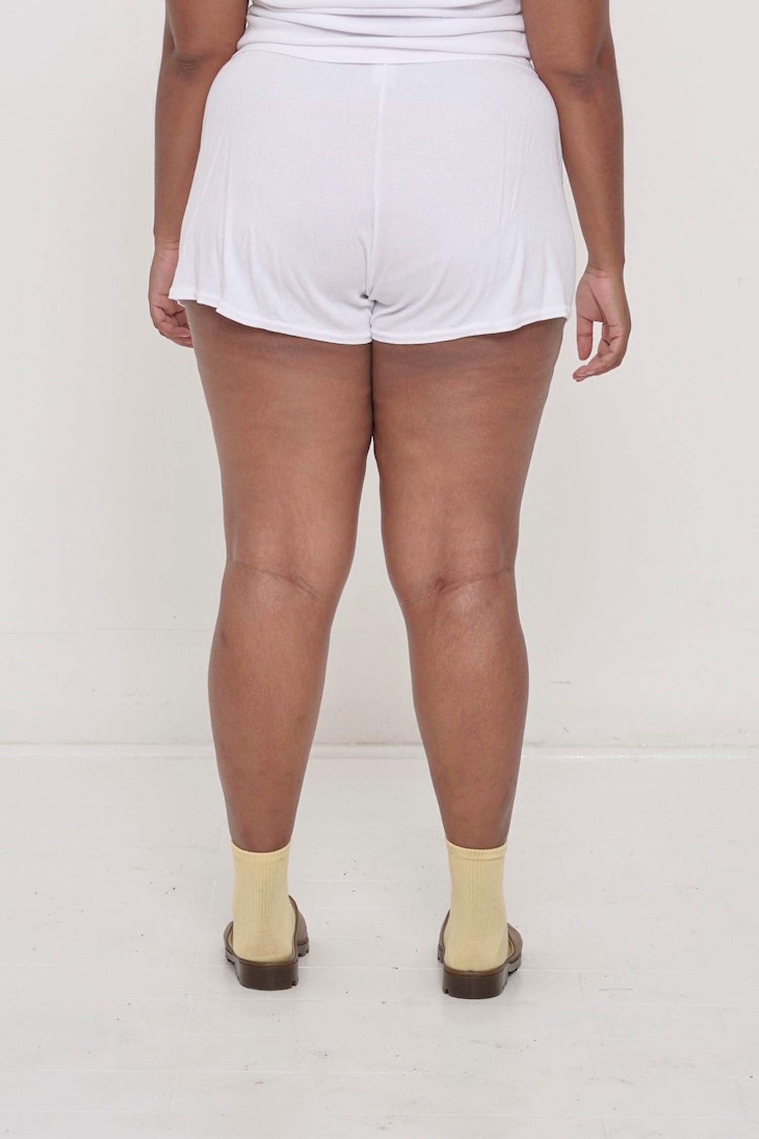 Back view: White Rib Shorts on a person, waist down. They feature a relaxed fit and a flowing, drapey fabric.