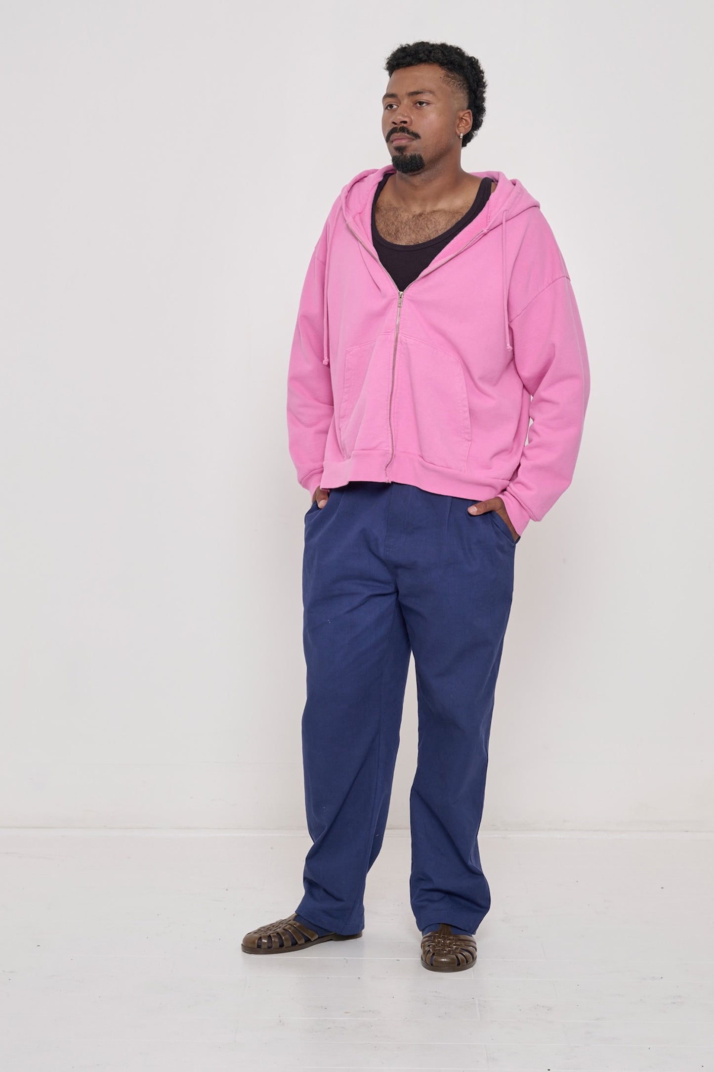 A man wearing a Mulberry Rib Tank, Pixie Trash Zip-Up Hoodie and Washed Navy Cotton Twill Life Uniform Pants.