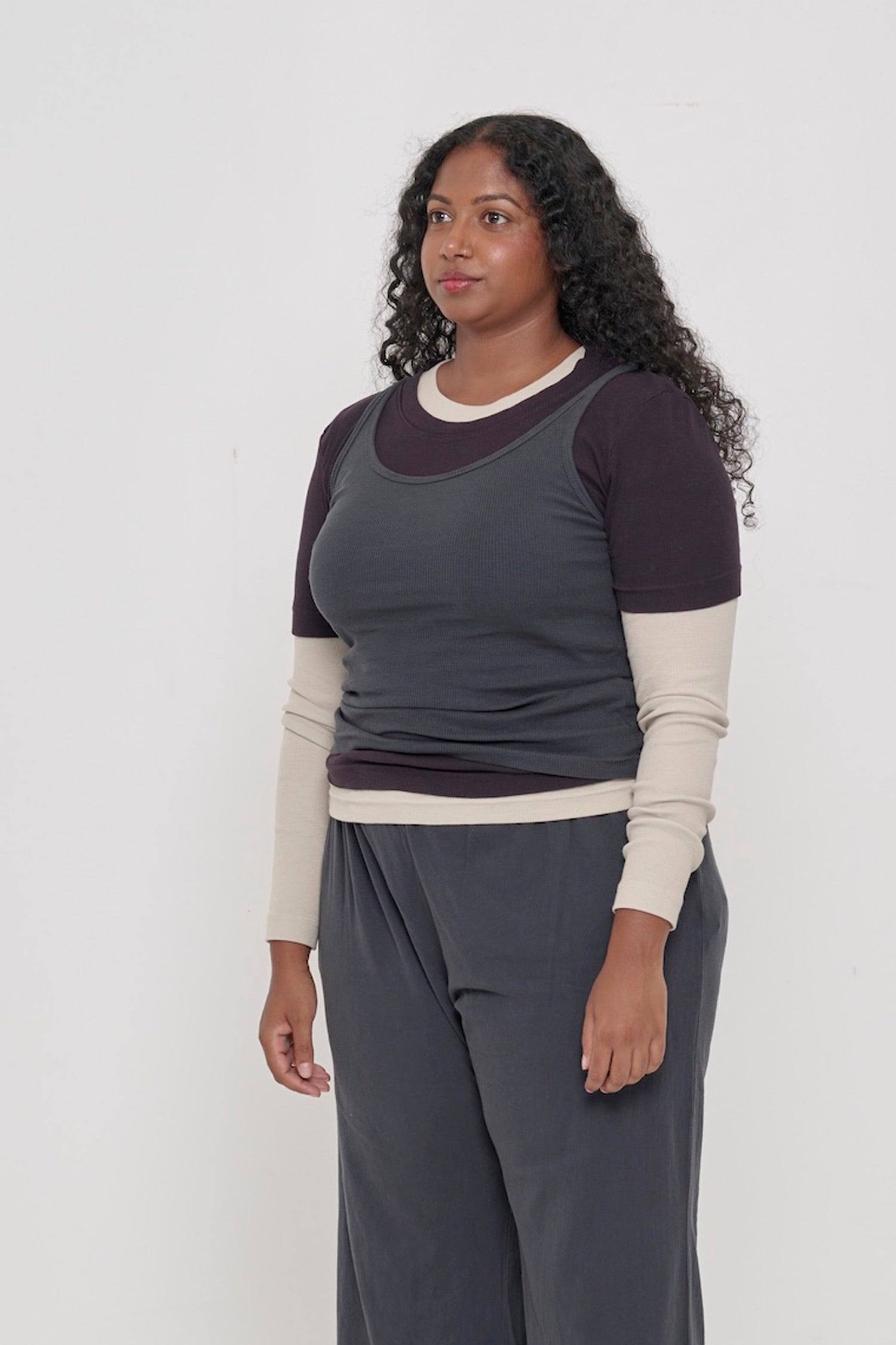 A person facing 45-degrees, wearing a Slate Rib Tank, showcasing heavy hem, and fitted silhouette.