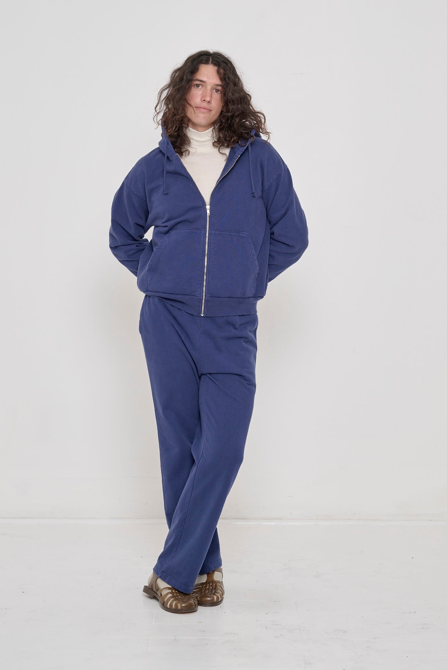 A person in a Washed Navy Trash Zip Up Hoodie and Apartment Pants, with the chest and collar of a Natural Rib Turtleneck visible.