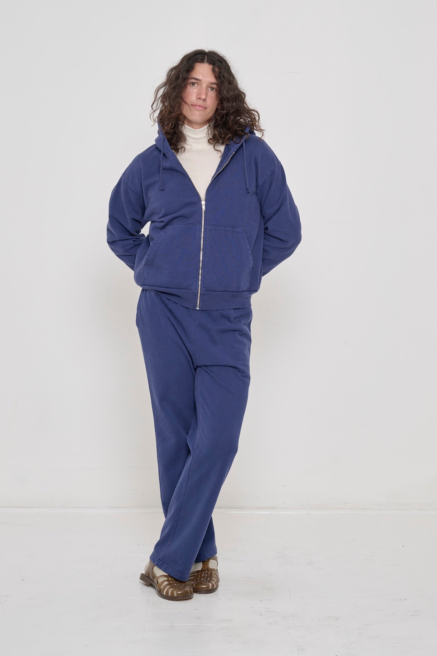 A person in a Washed Navy Trash Zip Up Hoodie and Apartment Pants, with the chest and collar of a Natural Rib Turtleneck visible.