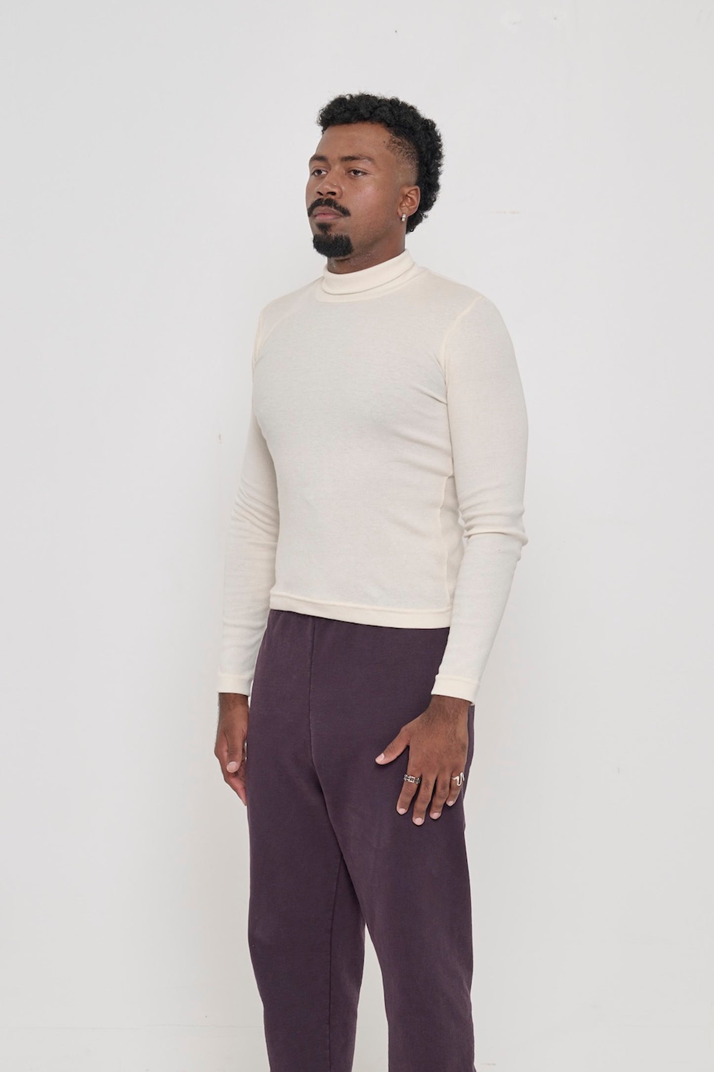 A Natural Rib Turtleneck on a person turned 45 degrees from the front, highlighting its form-fitting design and side seams.