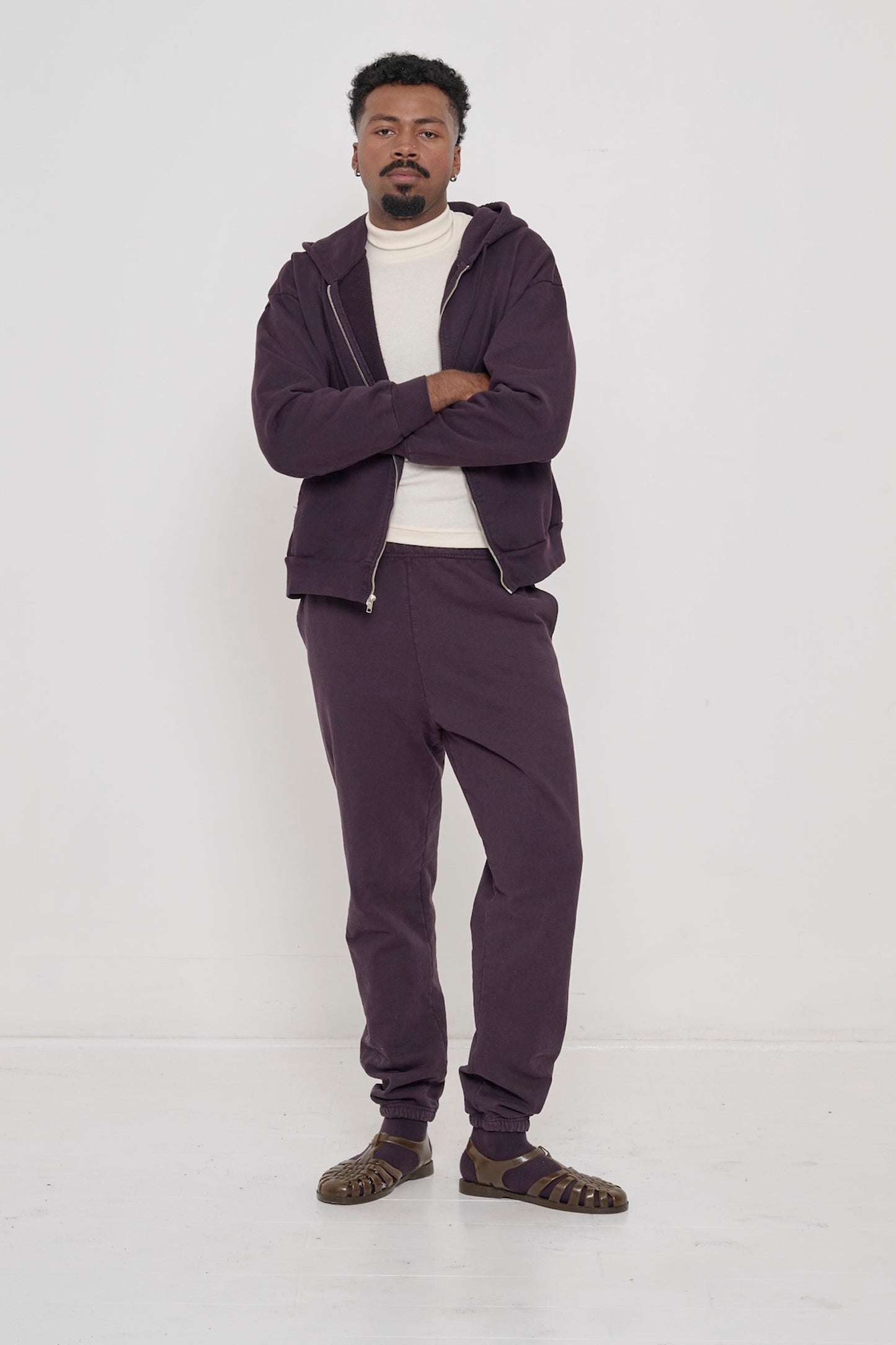 A person in an unzipped Mulberry Trash Zip Up Hoodie worn over a Natural Rib Turtleneck, with Mulberry Trash Sweatpants.