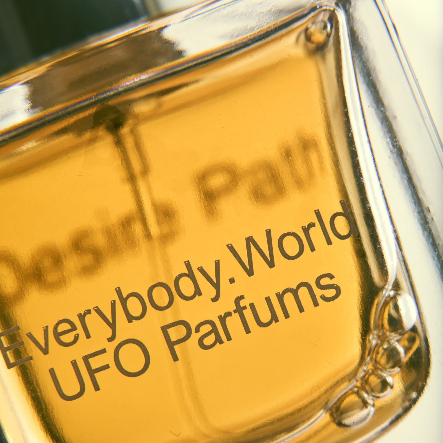 A close up image of our Desire Path eau de parfum, the juice looks rich amber in color and the bottle is branded with both Everybody.World and UFO Parfums