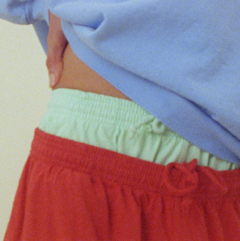 Close-up of a person wearing a Cielo Trash Crewneck, with their hand on their hip, and wearing layered Sea Glass and Cedar Everyday Shorts. 