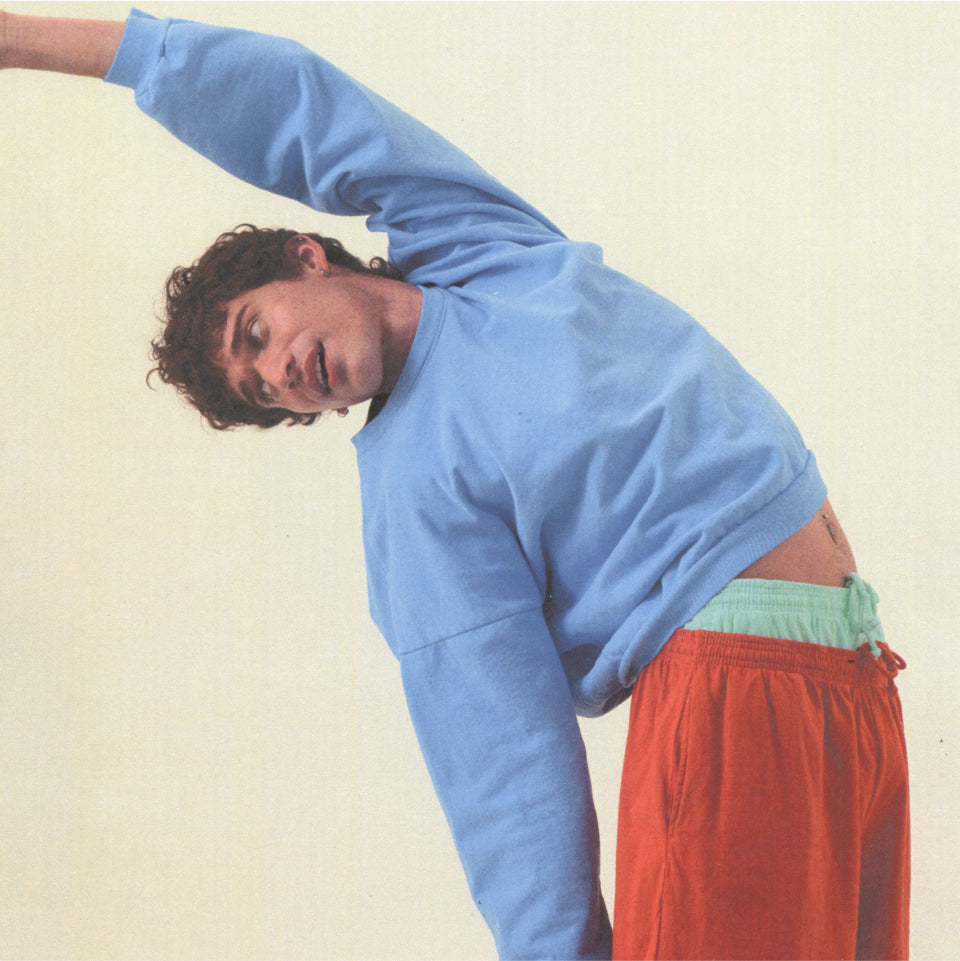 Model pictured stretching with our Trash Fleece Crewneck paired with layered Everyday Shorts in Cedar and Sea Glass