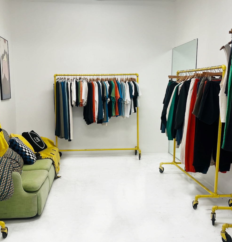 A couch and two bright yellow rolling racks filled with new arrivals, as seen inside the Everybody.World Informal Shop