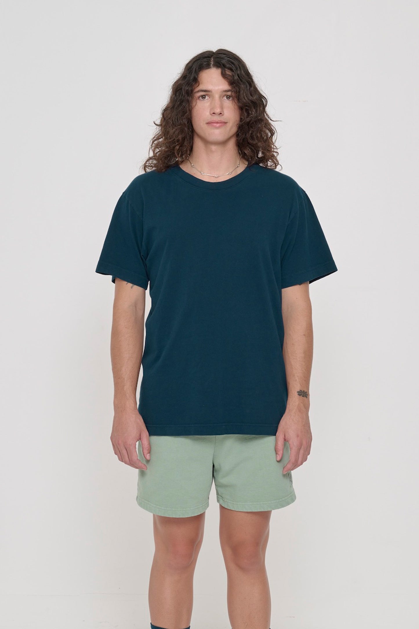 Front view of a person wearing the Short Sleeve Trash Tee in Juniper, showcasing its relaxed fit, hem hits below the hip.