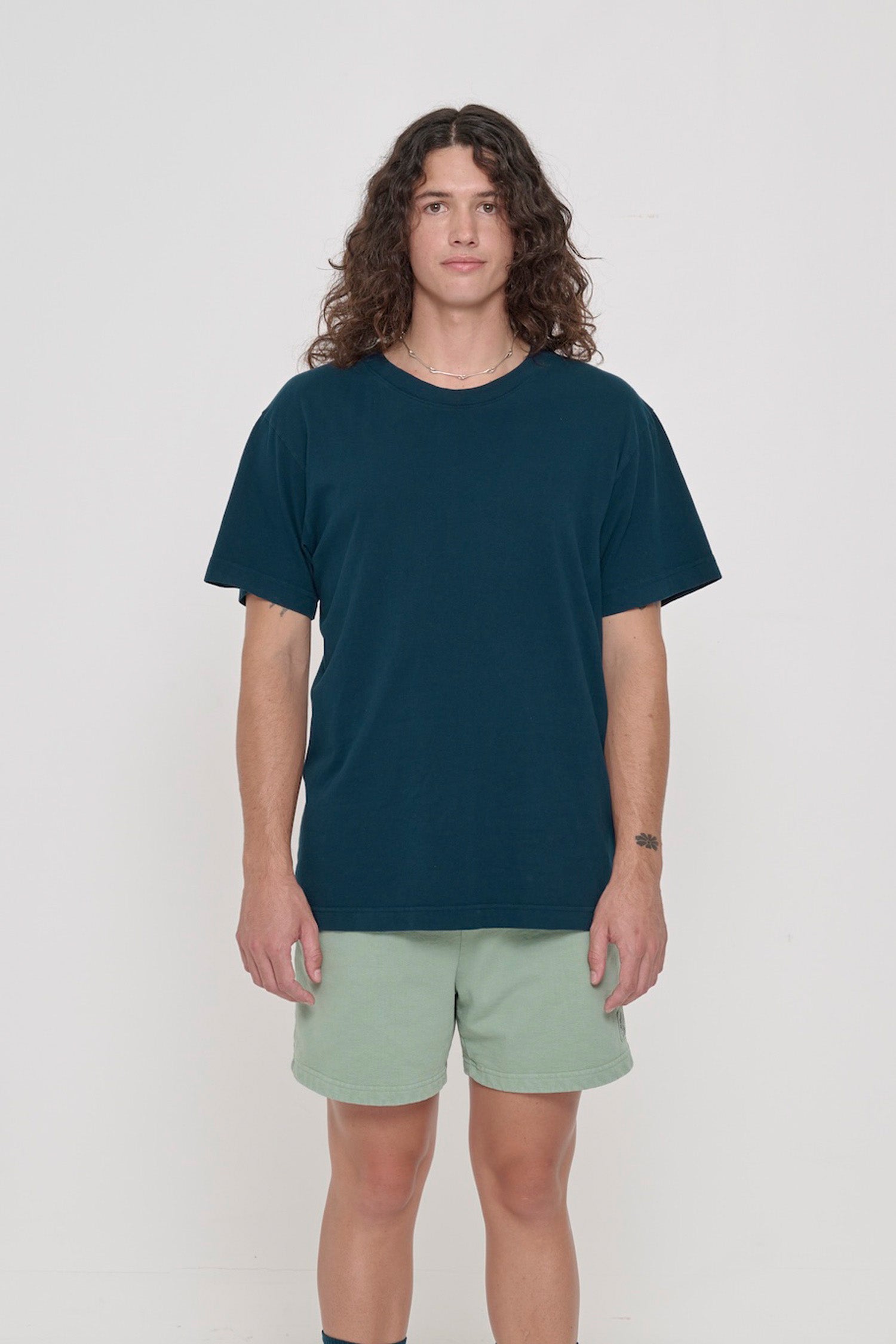 Front view of a person wearing the Short Sleeve Trash Tee in Juniper, showcasing its relaxed fit, hem hits below the hip.