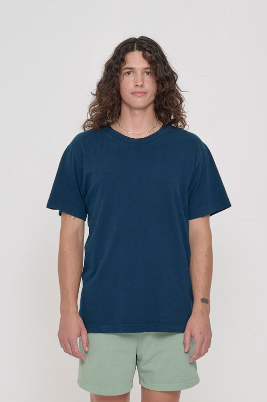 Front view of a person wearing the Short Sleeve Trash Tee in Juniper, showcasing its relaxed fit, hem hits below the hip.