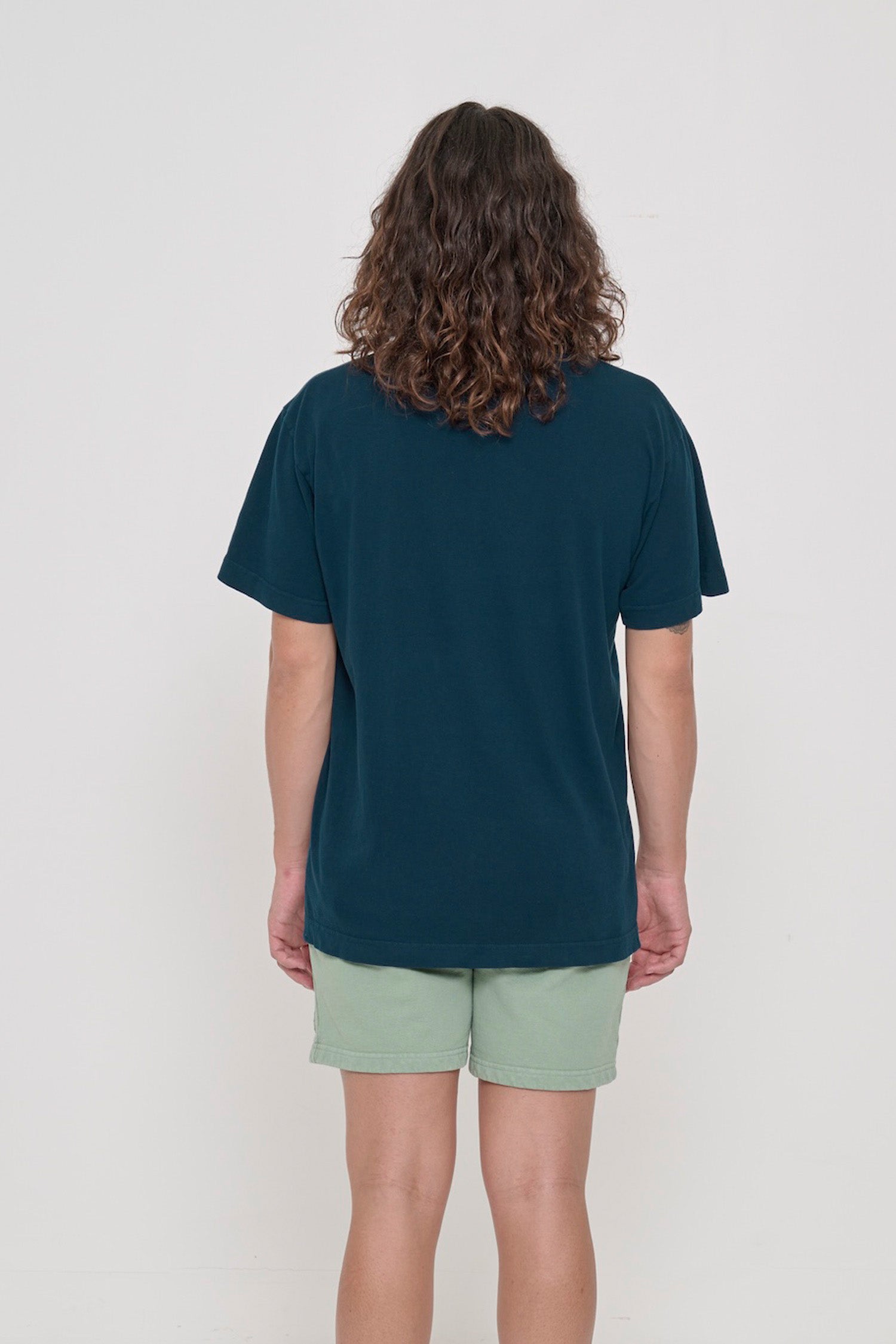Back view of a person wearing the Short Sleeve Trash Tee in Juniper, showing the relaxed slim body and wide sleeve.