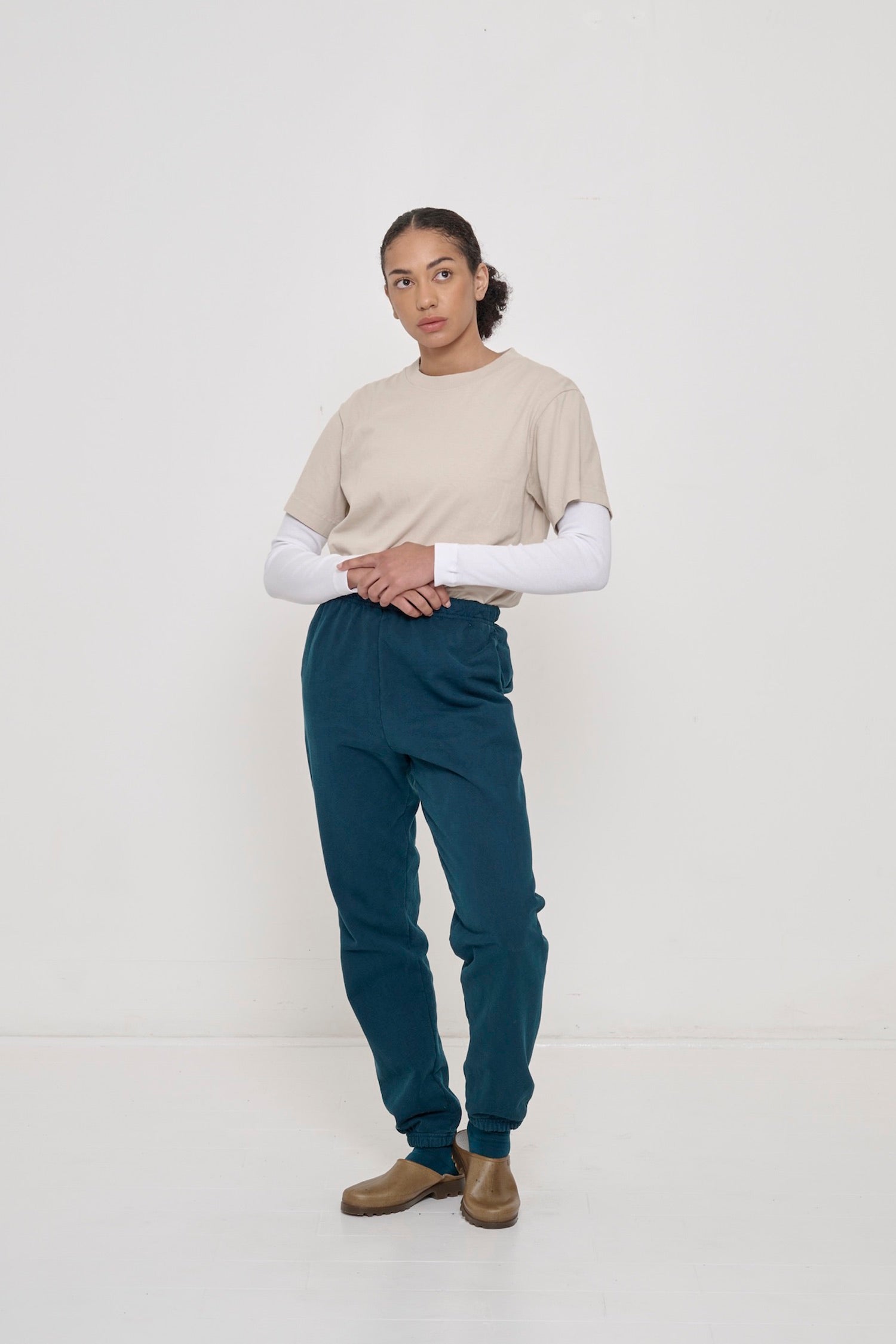 A woman wearing the Short Sleeve Trash Tee in Oat, layered over top of a White Rib Long Sleeve and Trash Sweatpants.