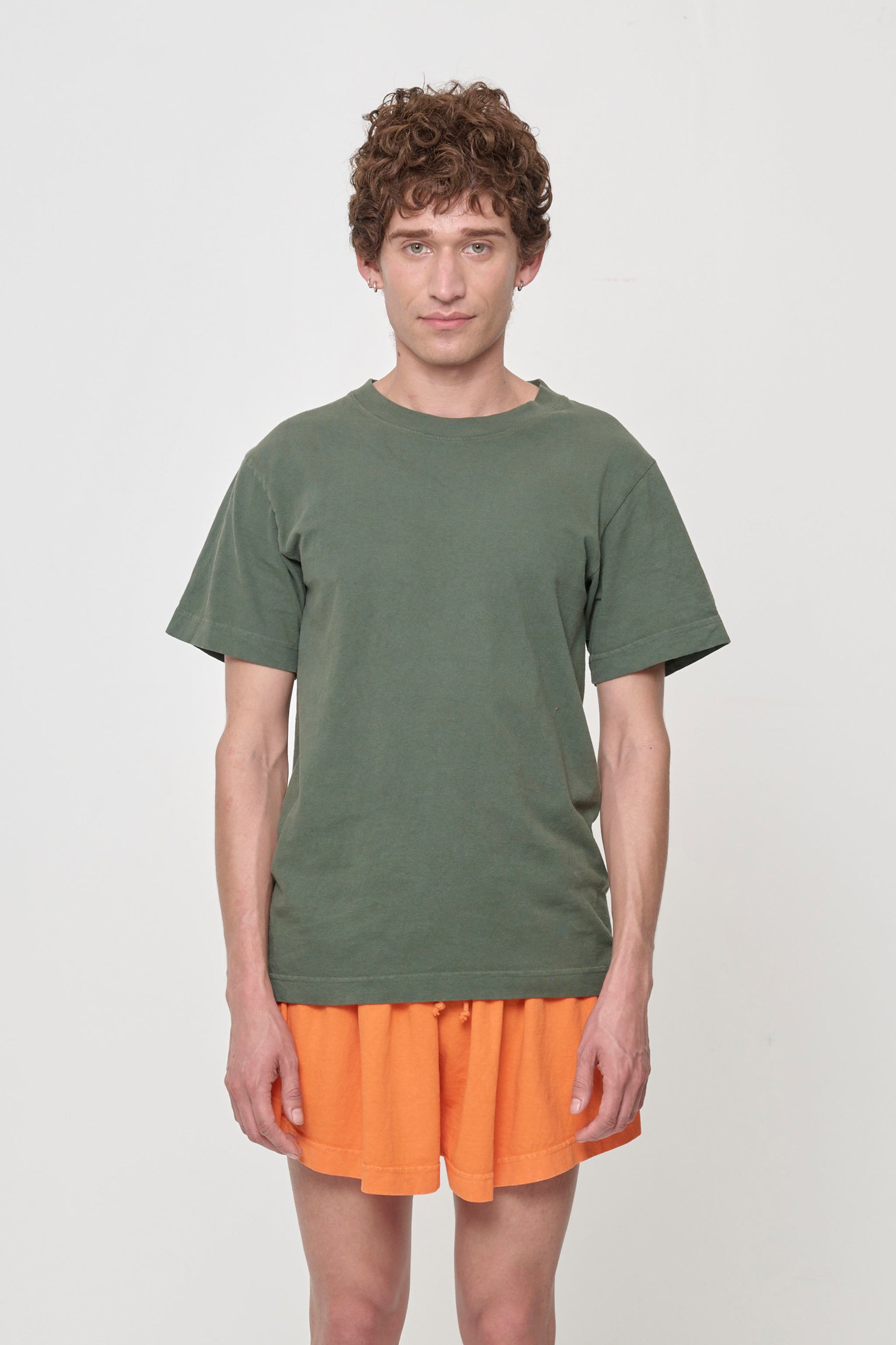 Front view of a non-binary model wearing the Short Sleeve Trash Tee in Pine, showcasing its relaxed fit and muted forest green color of Pine.