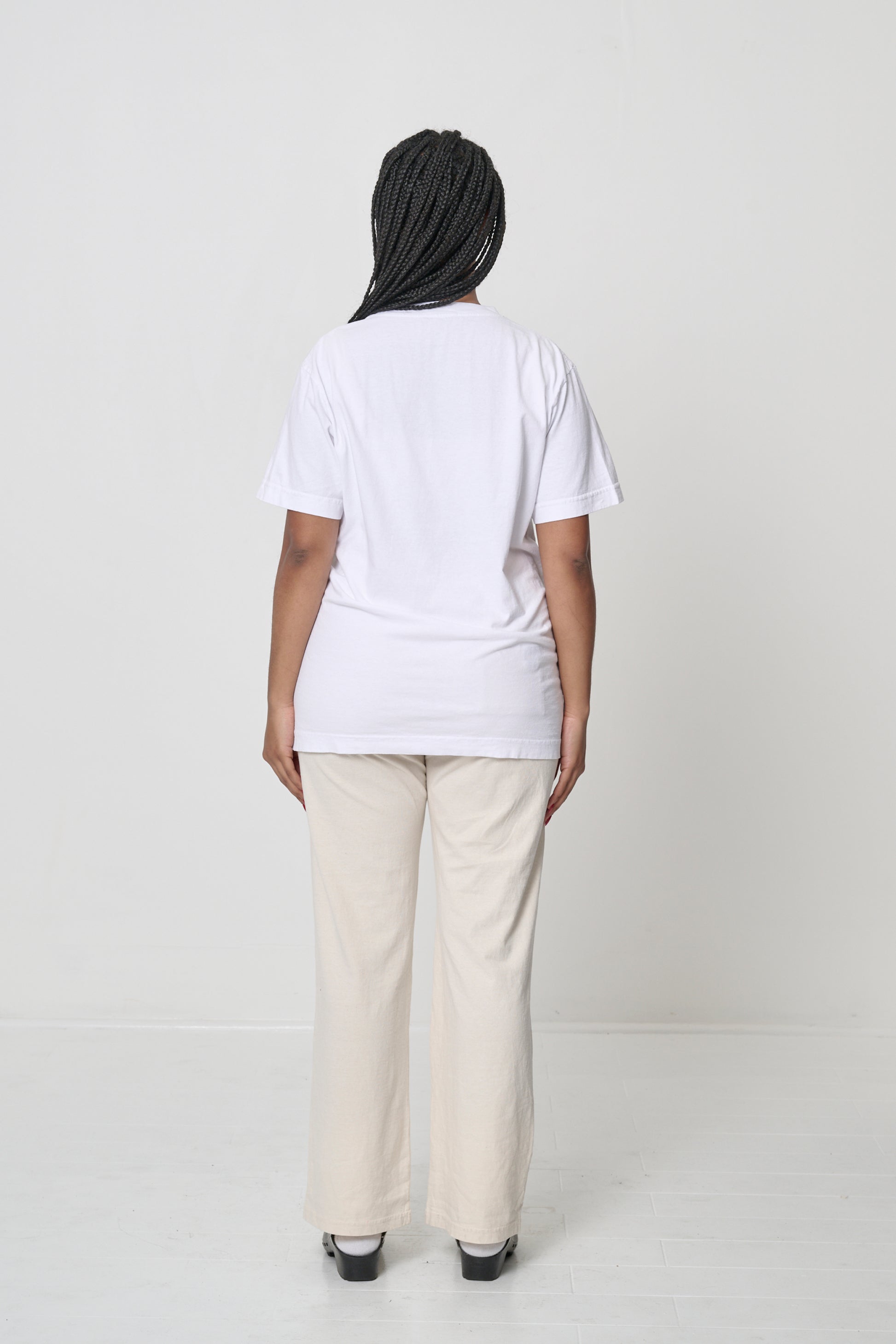 Back view: a woman in a White Short Sleeve Trash Tee, hair is pulled to the side showing the back neckline. 