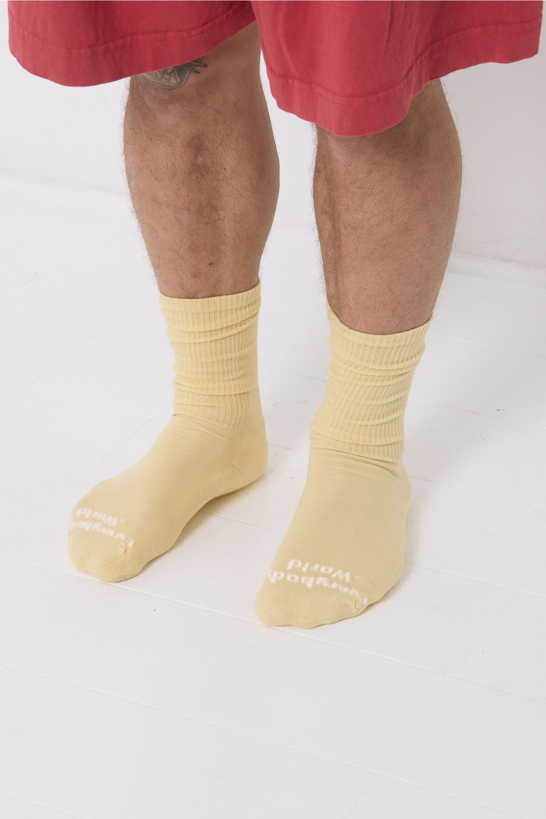 French Butter Squishy Socks, branded 'Everybody.World' in white at the toe, shown on a person's lower legs.
