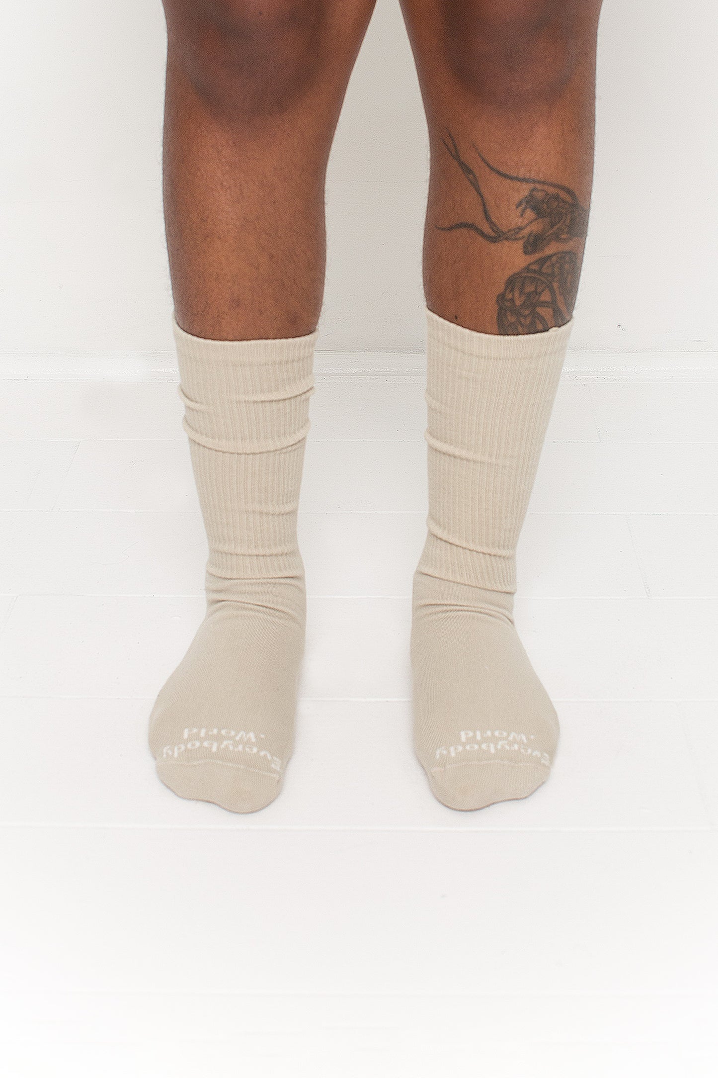 Oat Squishy Socks, branded 'Everybody.World' in white at the toe, shown on a person's lower legs.