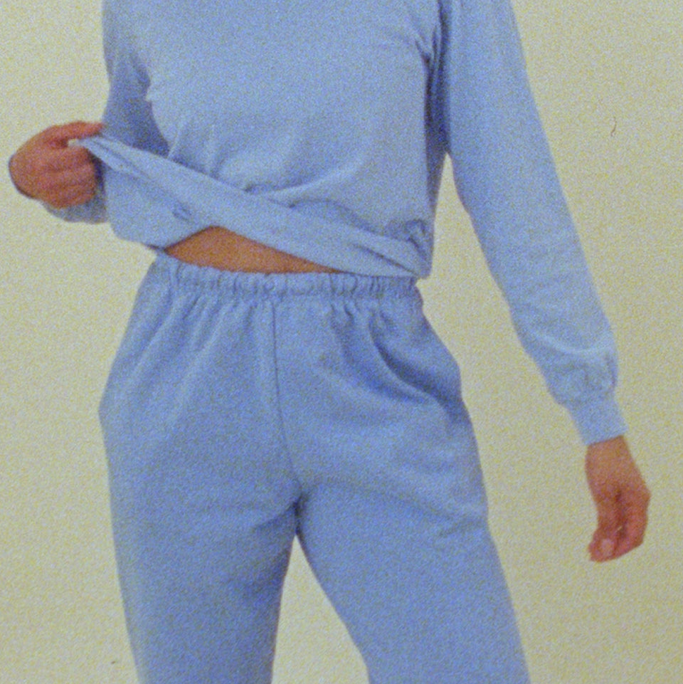 Person wearing a Trash Crewneck and Sweatpants in Cielo, sightly pulling up the bottom of the crewneck with their hand.