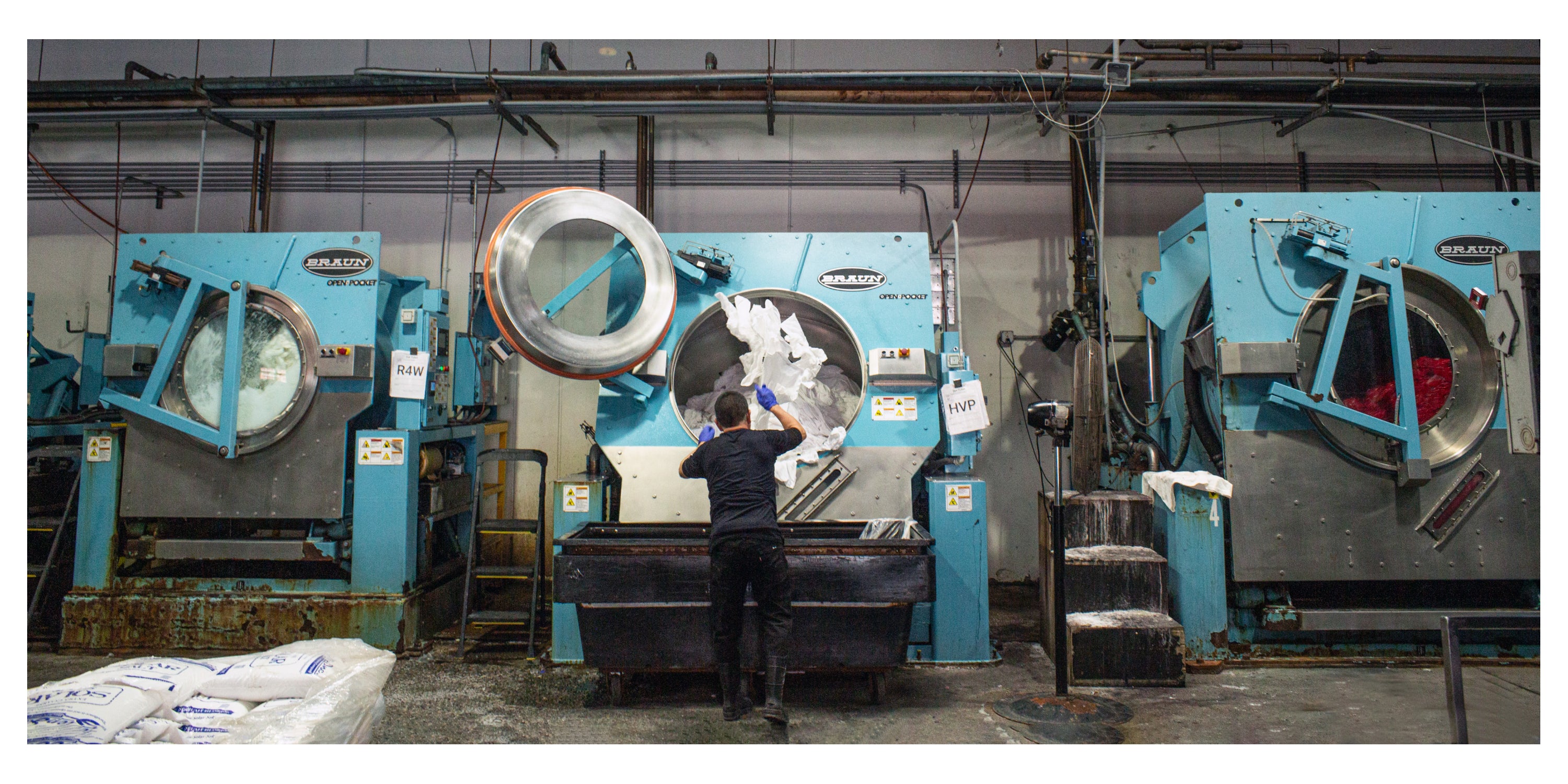 Person throwing white T-shirts into a large industrial washing machine.