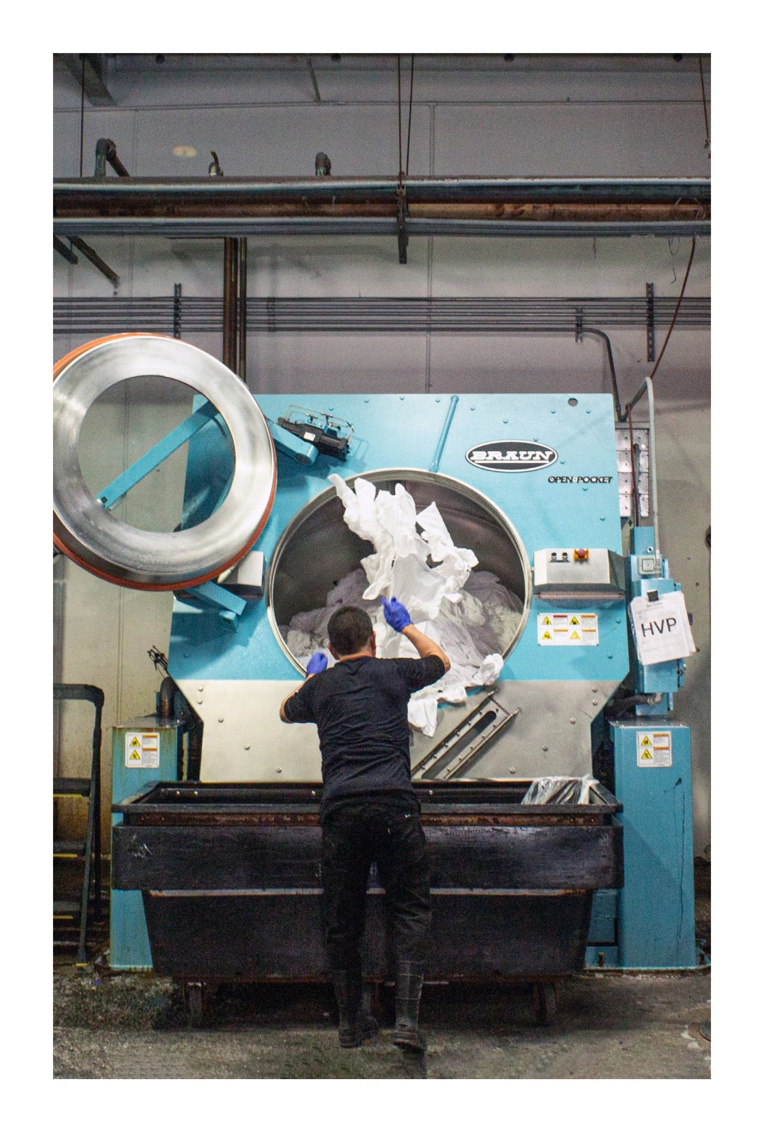 Person throwing white T-shirts into a large industrial washing machine.