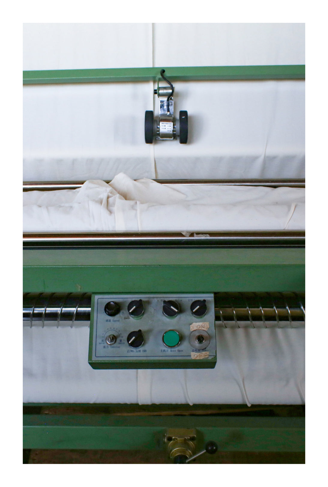 Close up on part of a green textile machine with white fabric.