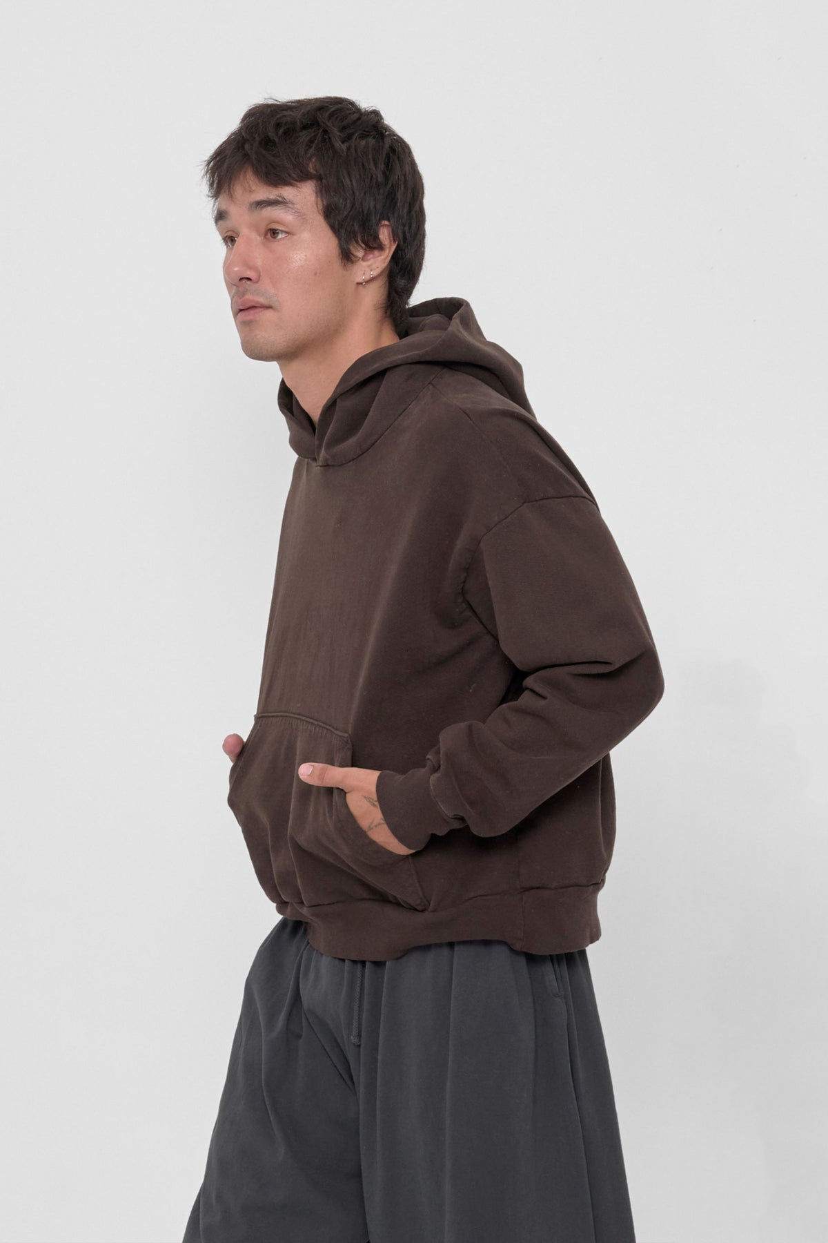 Trash Hoodie in Wet Soil – side view, model's hands in kangaroo pockets