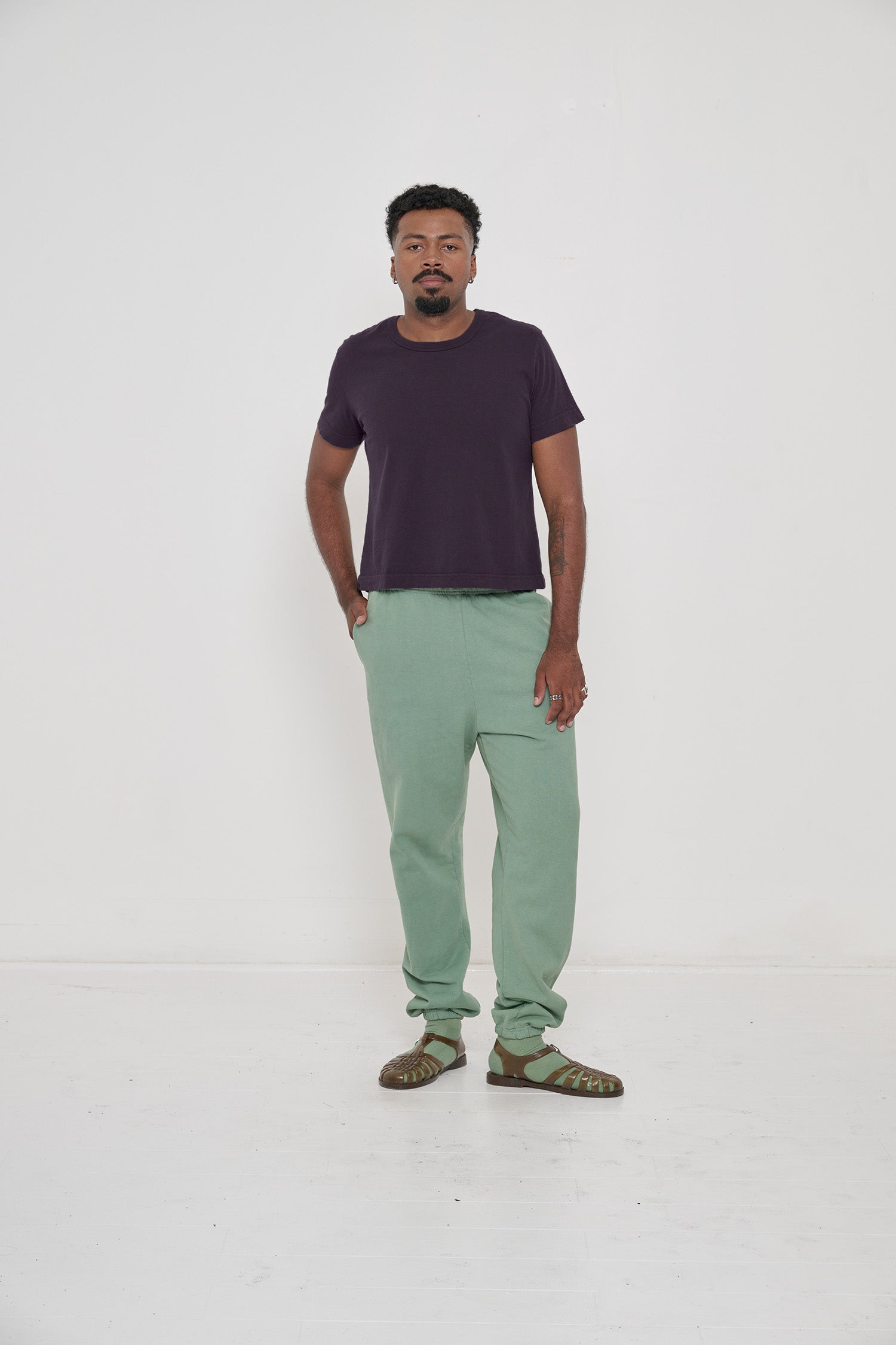 Man in Mulberry Tailored Trash Tee and Wasabi Trash Sweatpants, one hand in pocket, showing shirt's slim sleeves.