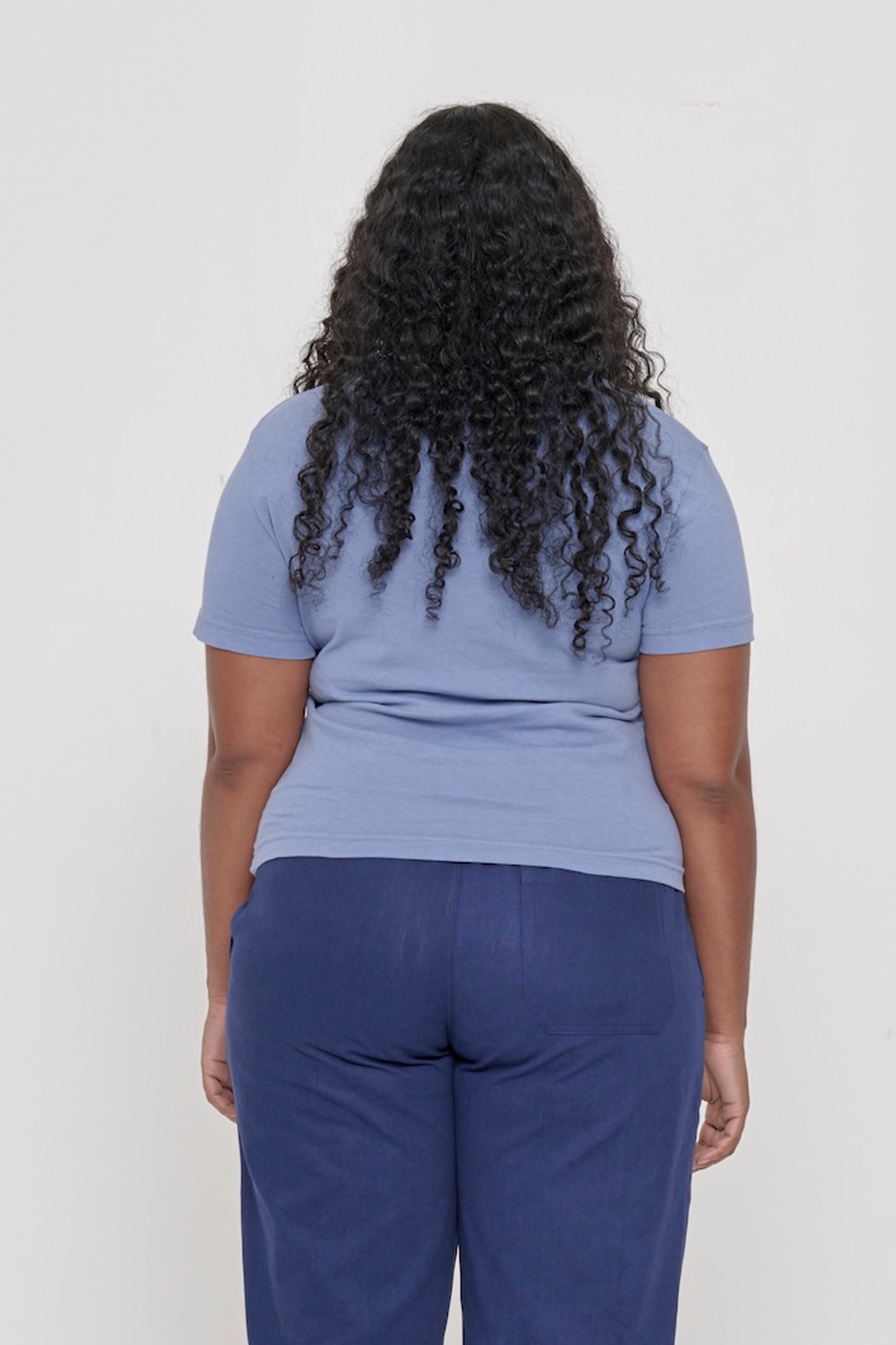 Back view: woman in a Periwinkle Tailored Trash Tee. Fitted throughout.