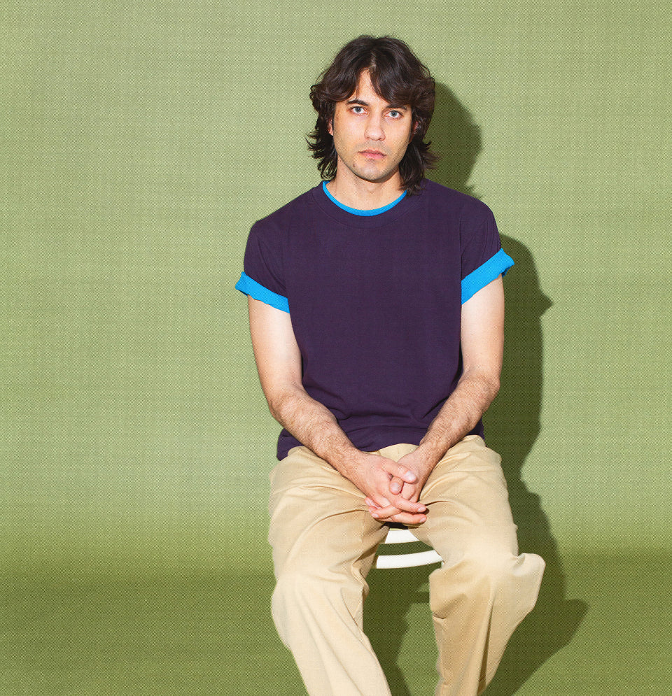 Man sitting, wearing Boxier Trash Tee in Mulberry and Malibu, with Sandstorm Life Uniform Pants.