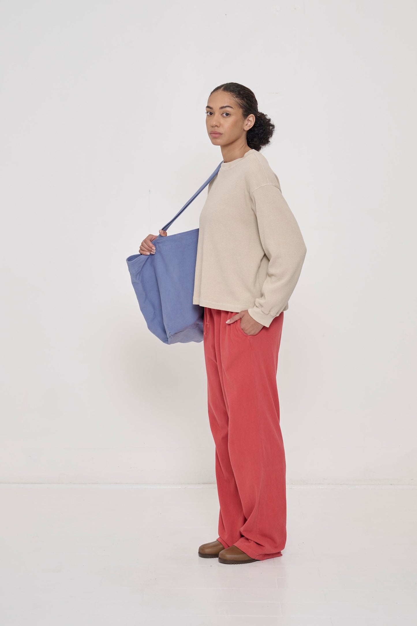A woman in Oat Thermal Long Sleeve Boxier Trash Tee, Cedar Apartment Pants, and Periwinkle Big Tote over her shoulder. 