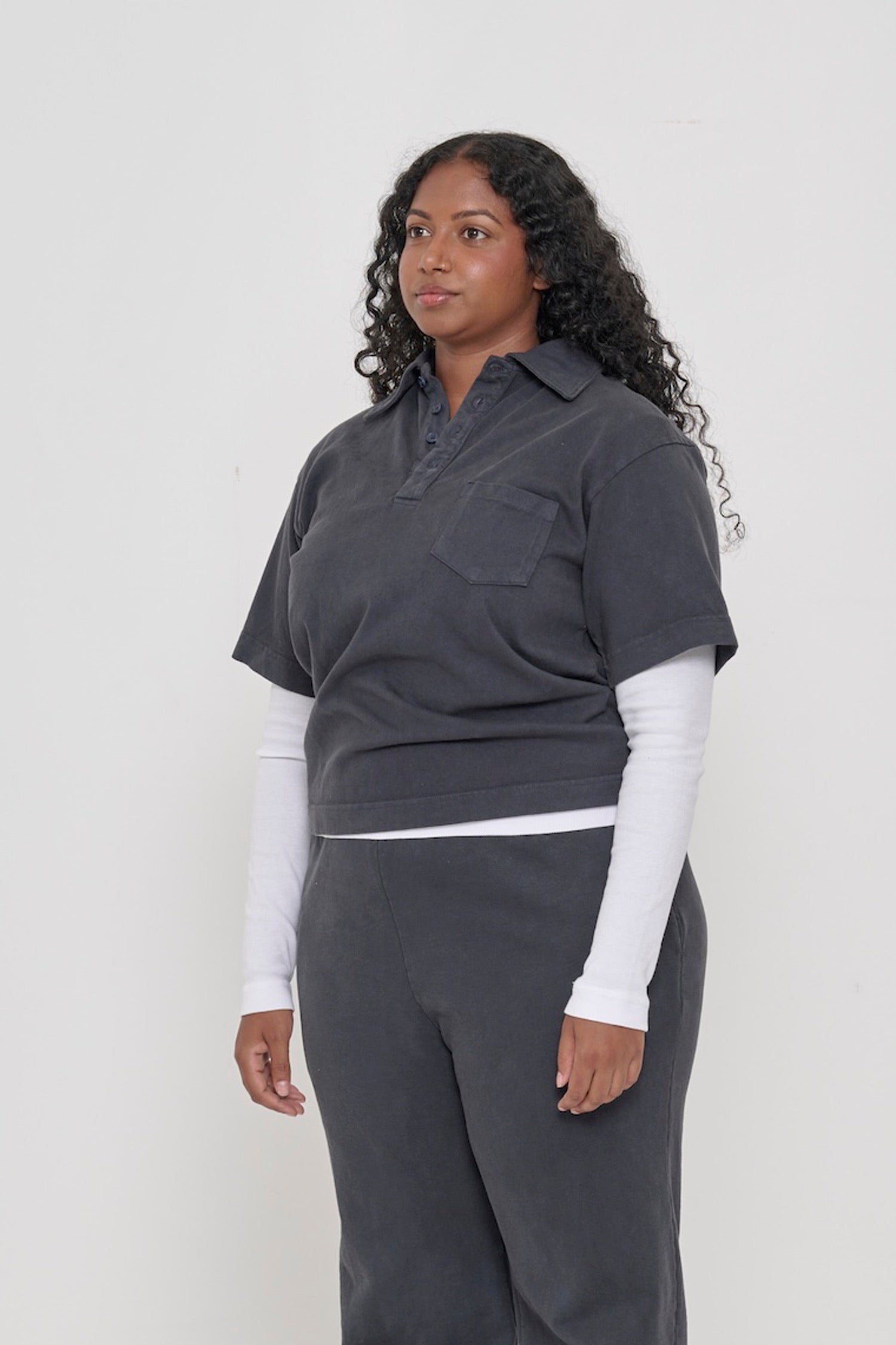 Woman turned 45 degrees, wearing a Slate Trash Polo, featuring short sleeves and left chest pocket.