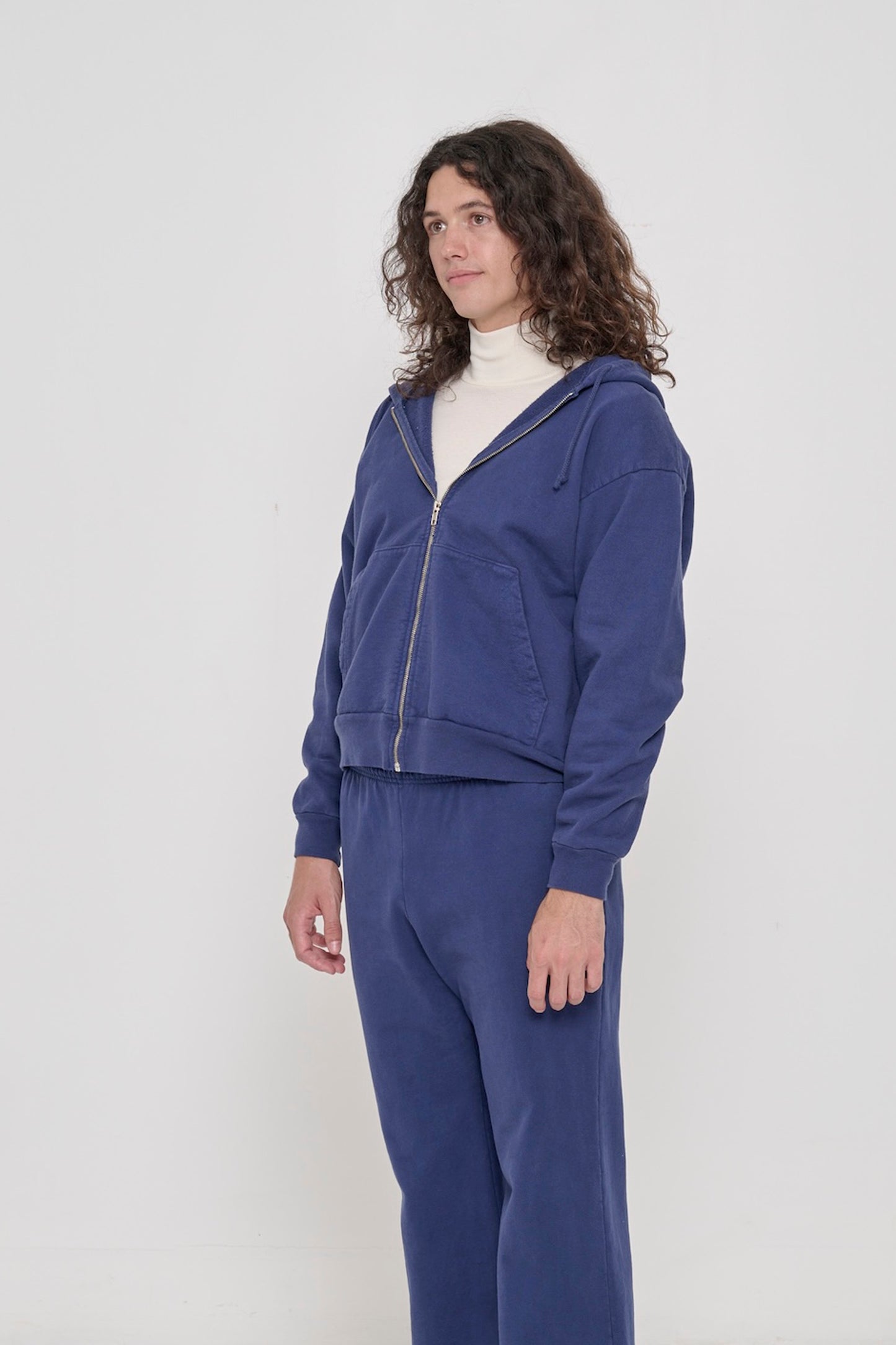 A person facing 45-degrees, in a Washed Navy Trash Zip Up Hoodie, showcasing sleeve's relaxed fit and drop shoulder.