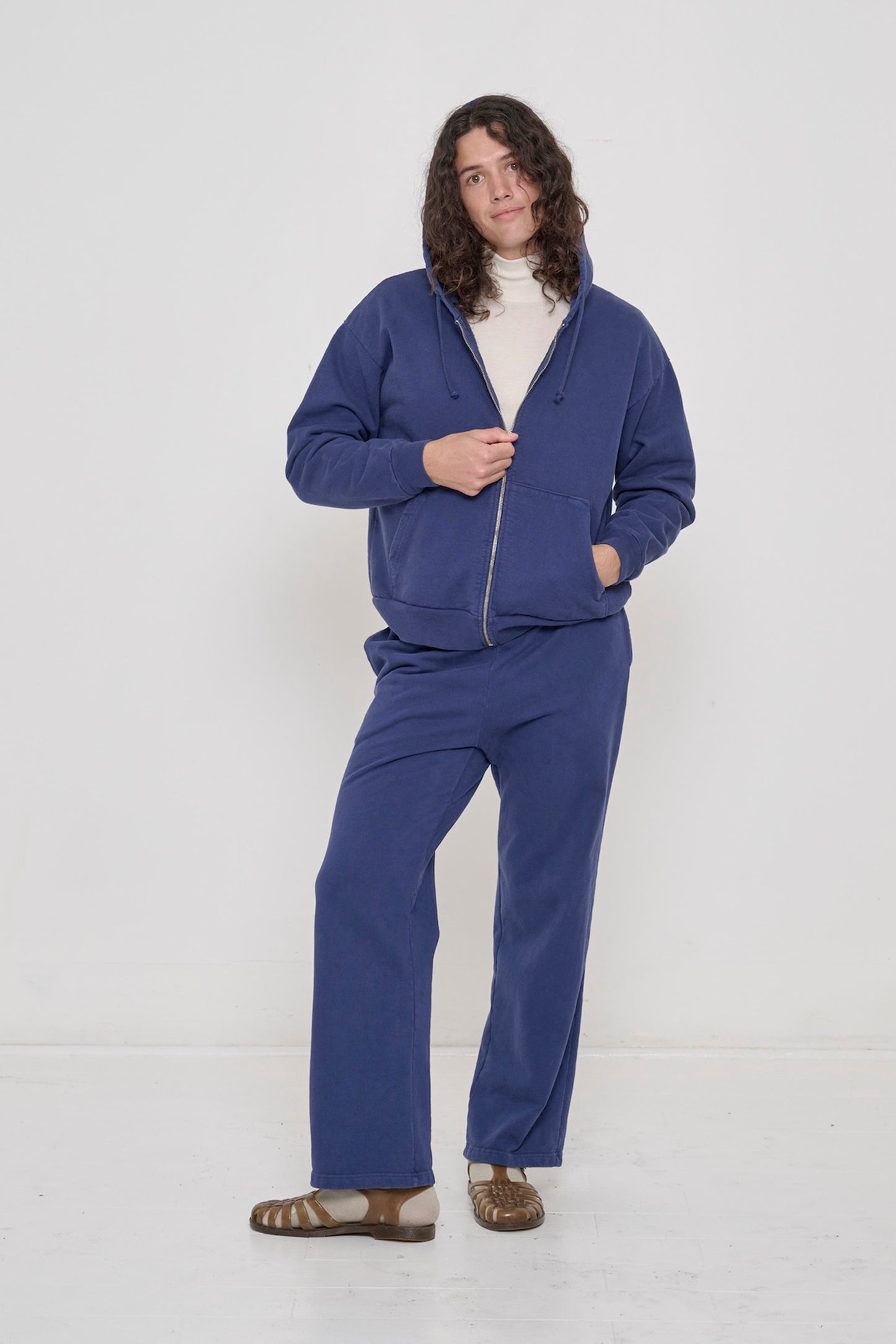 Person in Washed Navy Trash Zip Up Hoodie, hood up, hand on half-zipped zipper, other hand in kangaroo pocket.