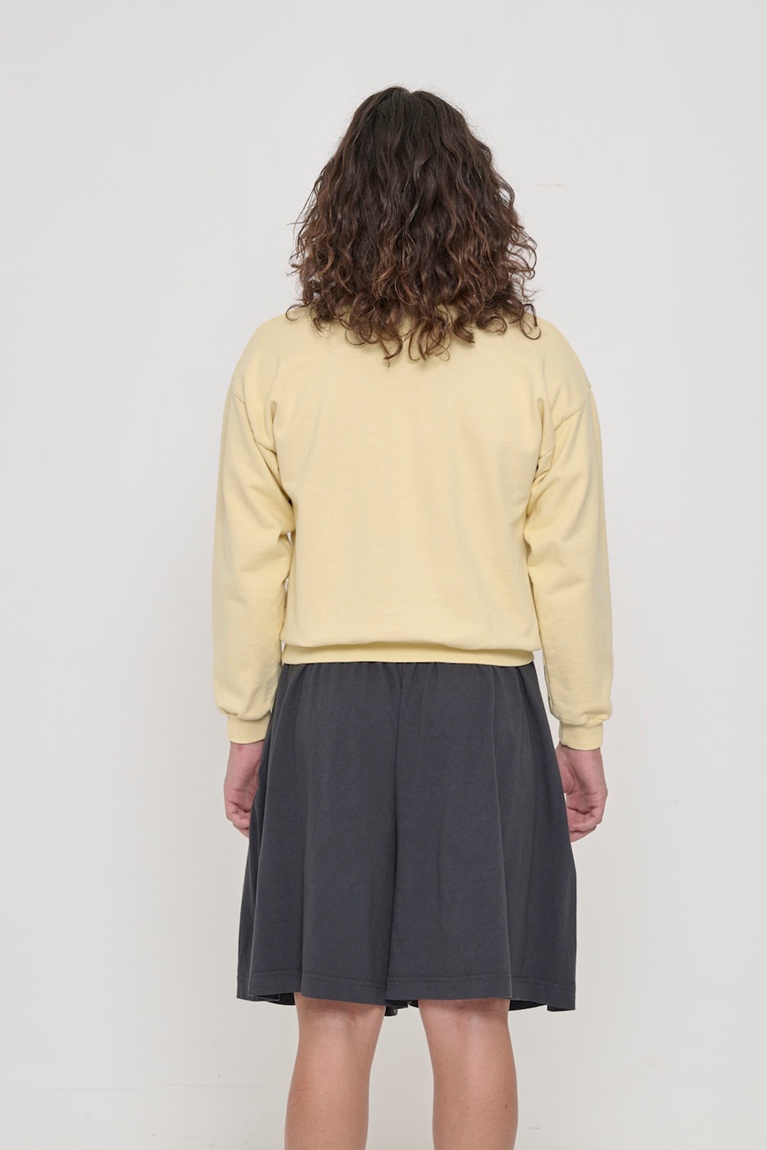 Back view on a person in French Butter Trash Crewneck, relaxed throughout until the rib hem and cuffs.