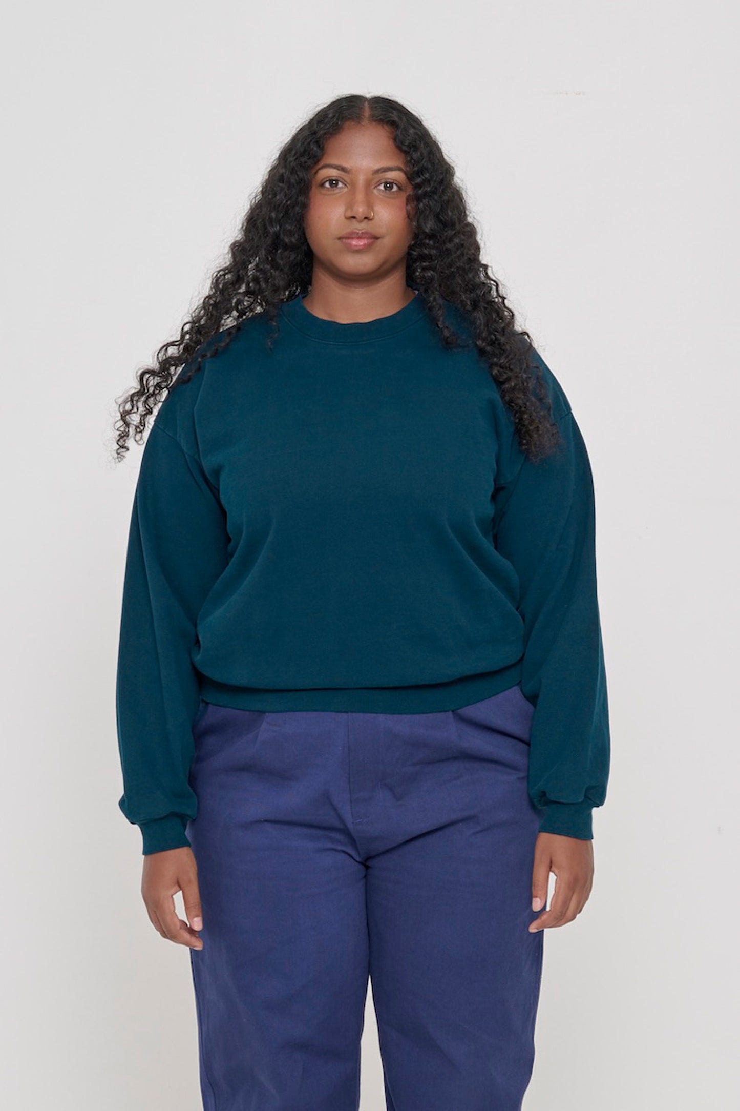 Front view of a person wearing Juniper Trash Crewneck. Hem hits their upper hip.