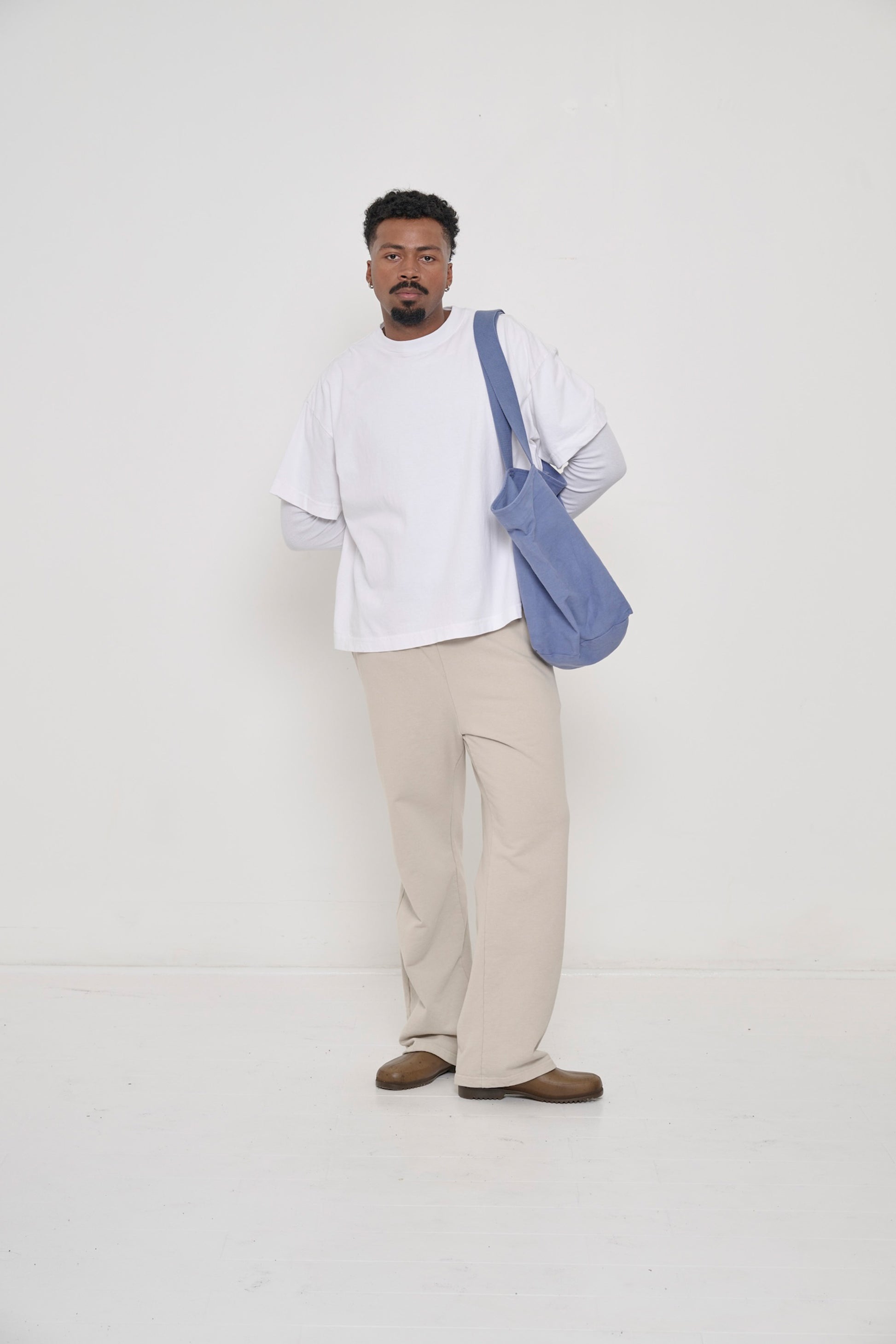A person wearing Trash Fleece Apartment Pants in Oat and Heavyweight Boxier Trash Tee in White.