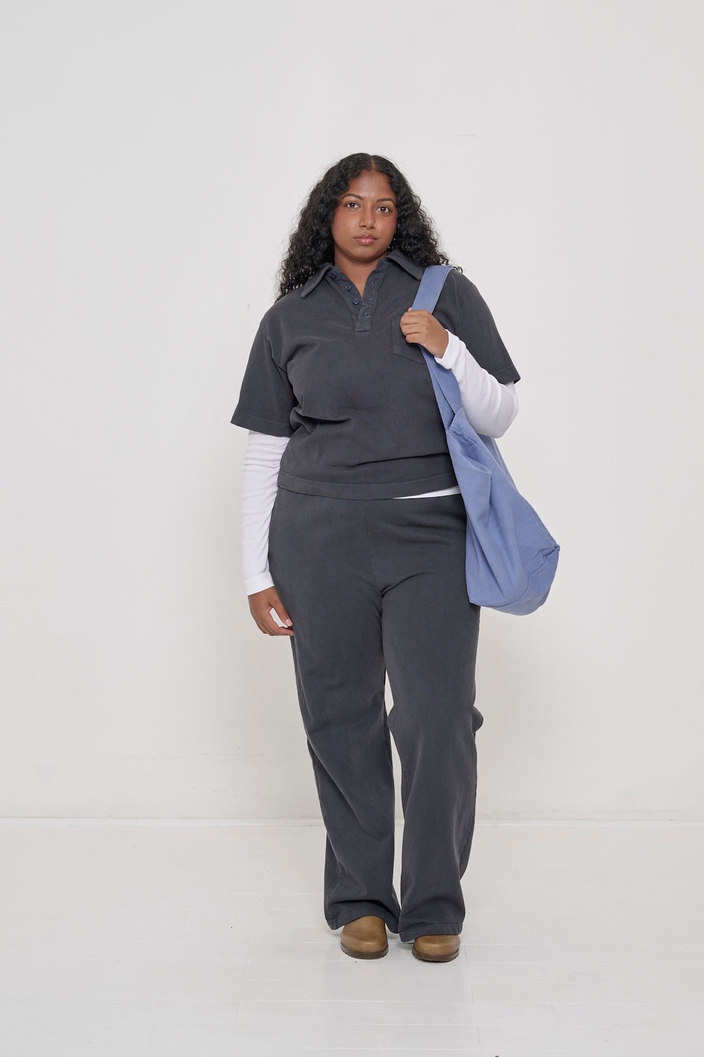 A woman wearing Trash Fleece Apartment Pants in Slate and carrying the Periwinkle Big Tote.
