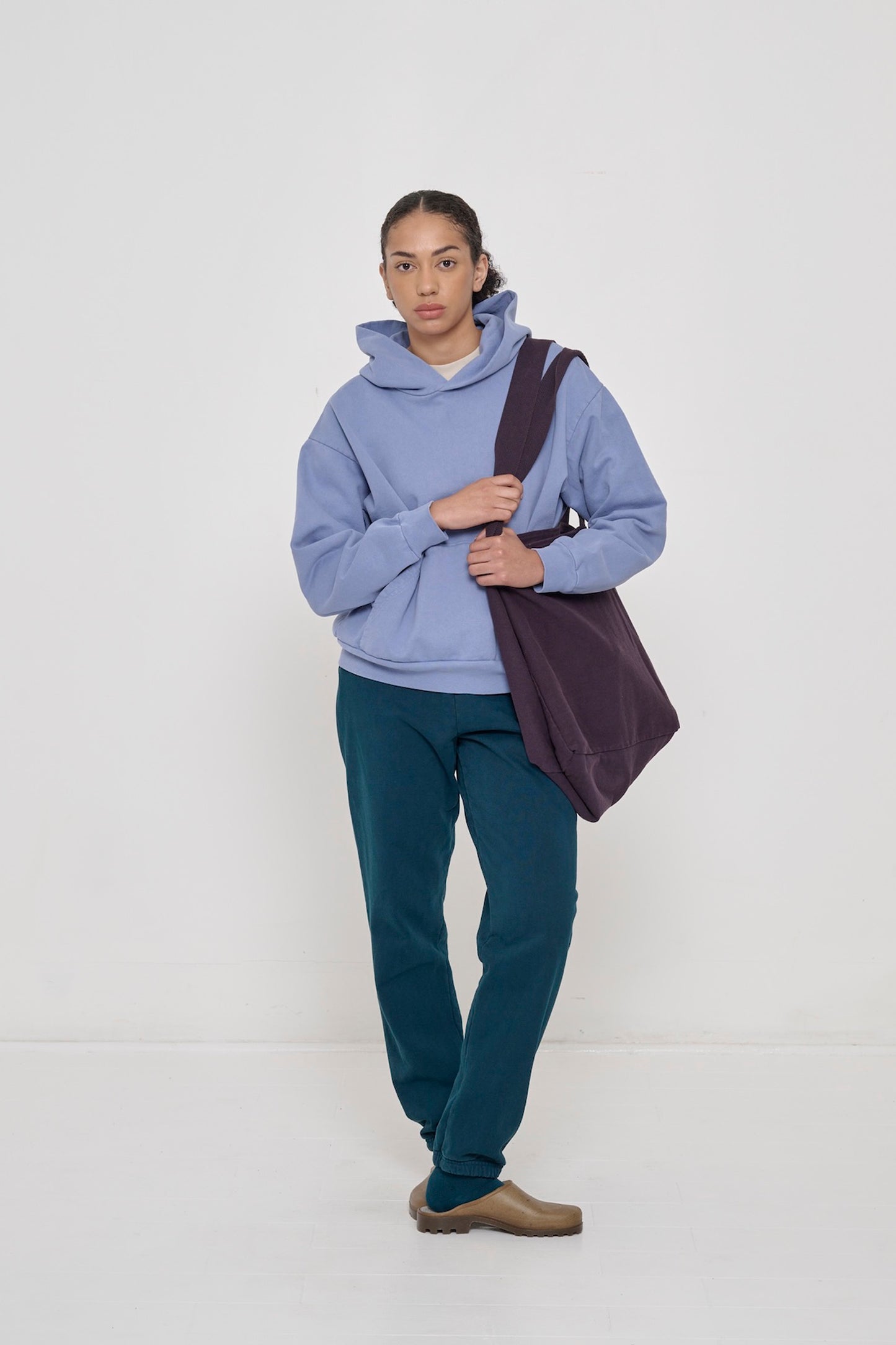 Woman wearing a Periwinkle Trash Hoodie with Mulberry Big Tote and Juniper Trash Sweatpants.
