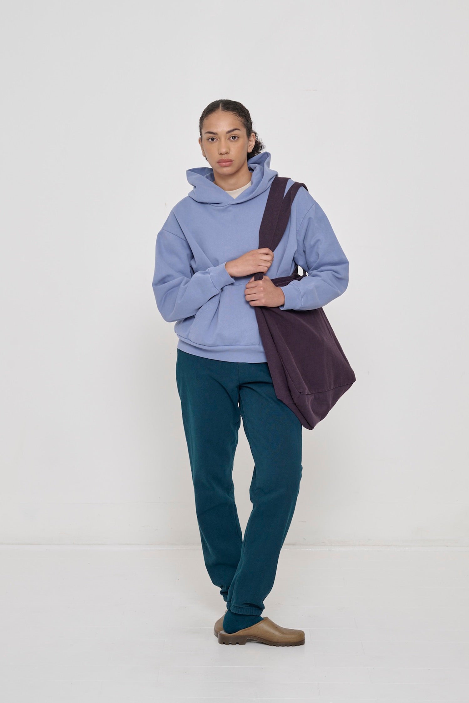 Woman wearing a Periwinkle Trash Hoodie with Mulberry Big Tote and Juniper Trash Sweatpants.