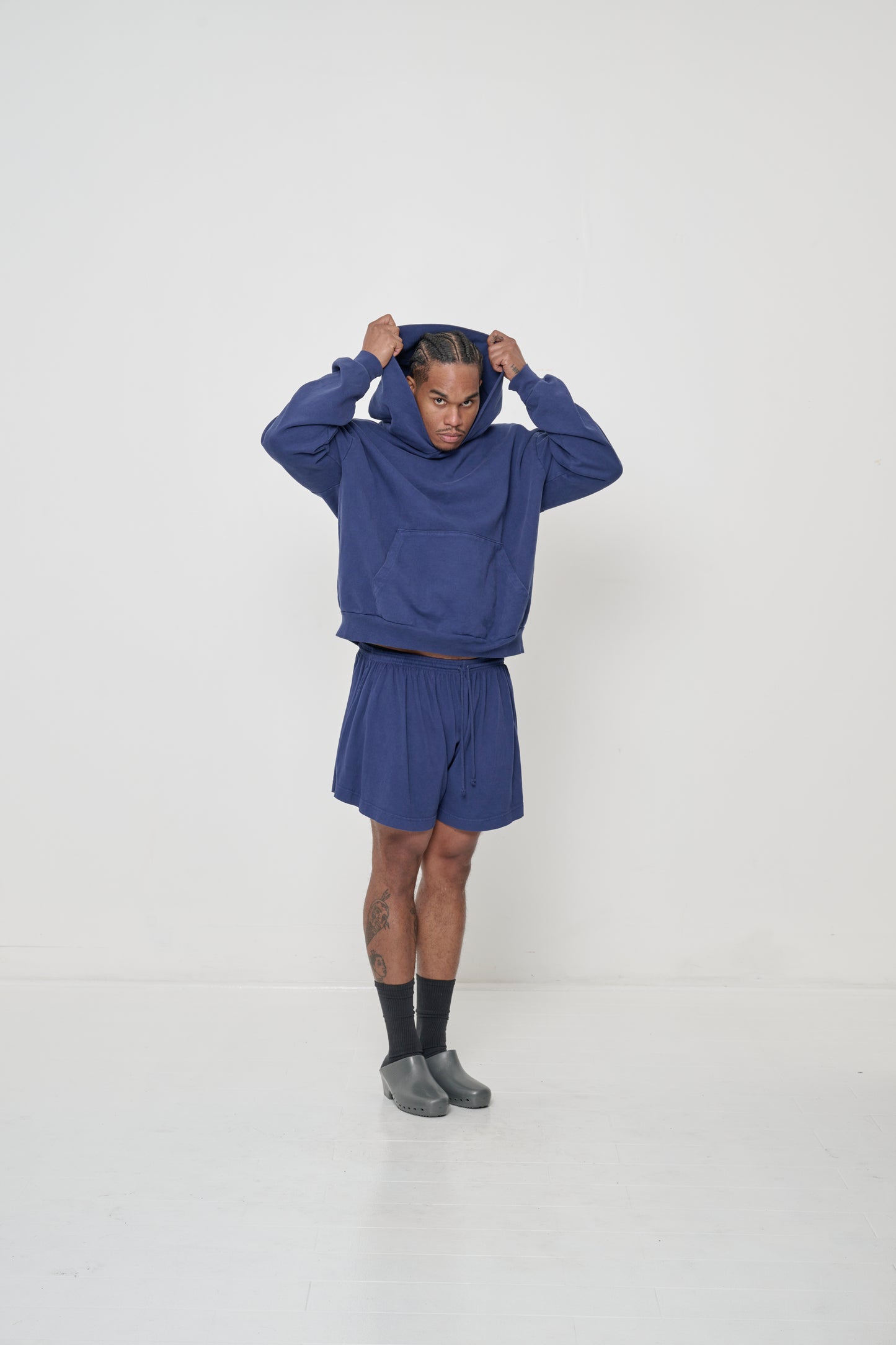 Profile full length view: man wearing a Washed Navy Trash Hoodie with hands pulling the hood over his head.