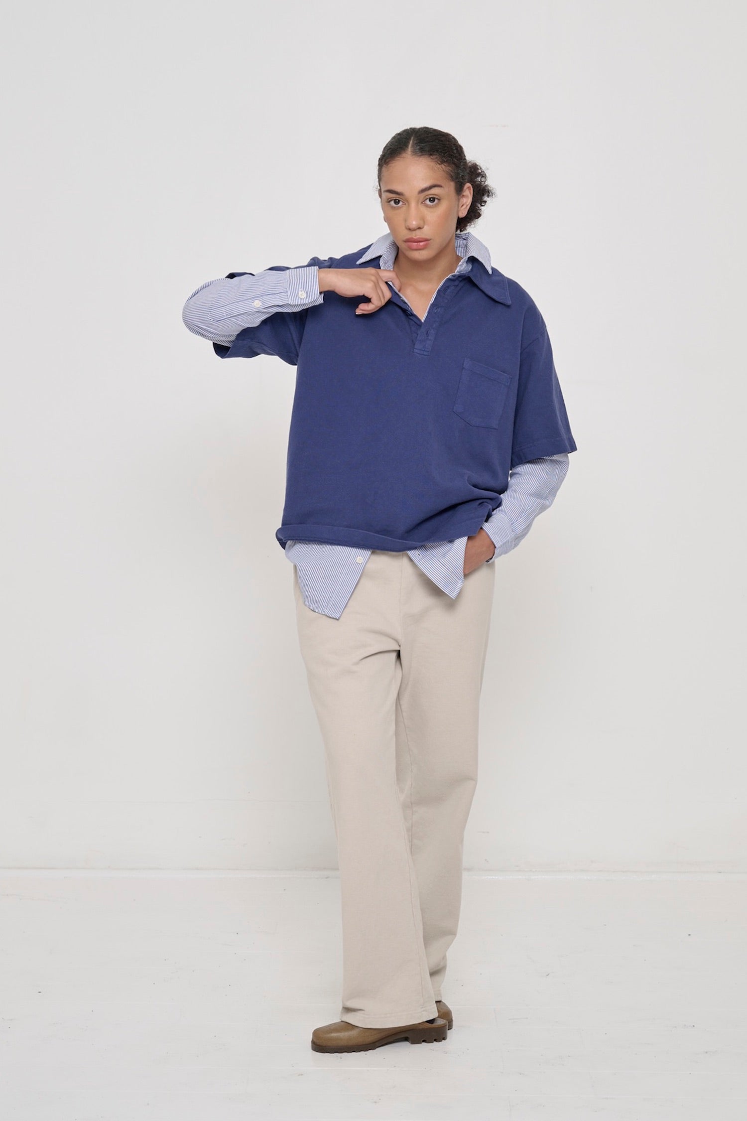 Woman wearing Washed Navy Trash Polo with a Stripe Poplin Button-Up Shirt underneath and Trash Fleece Apartment Pants.