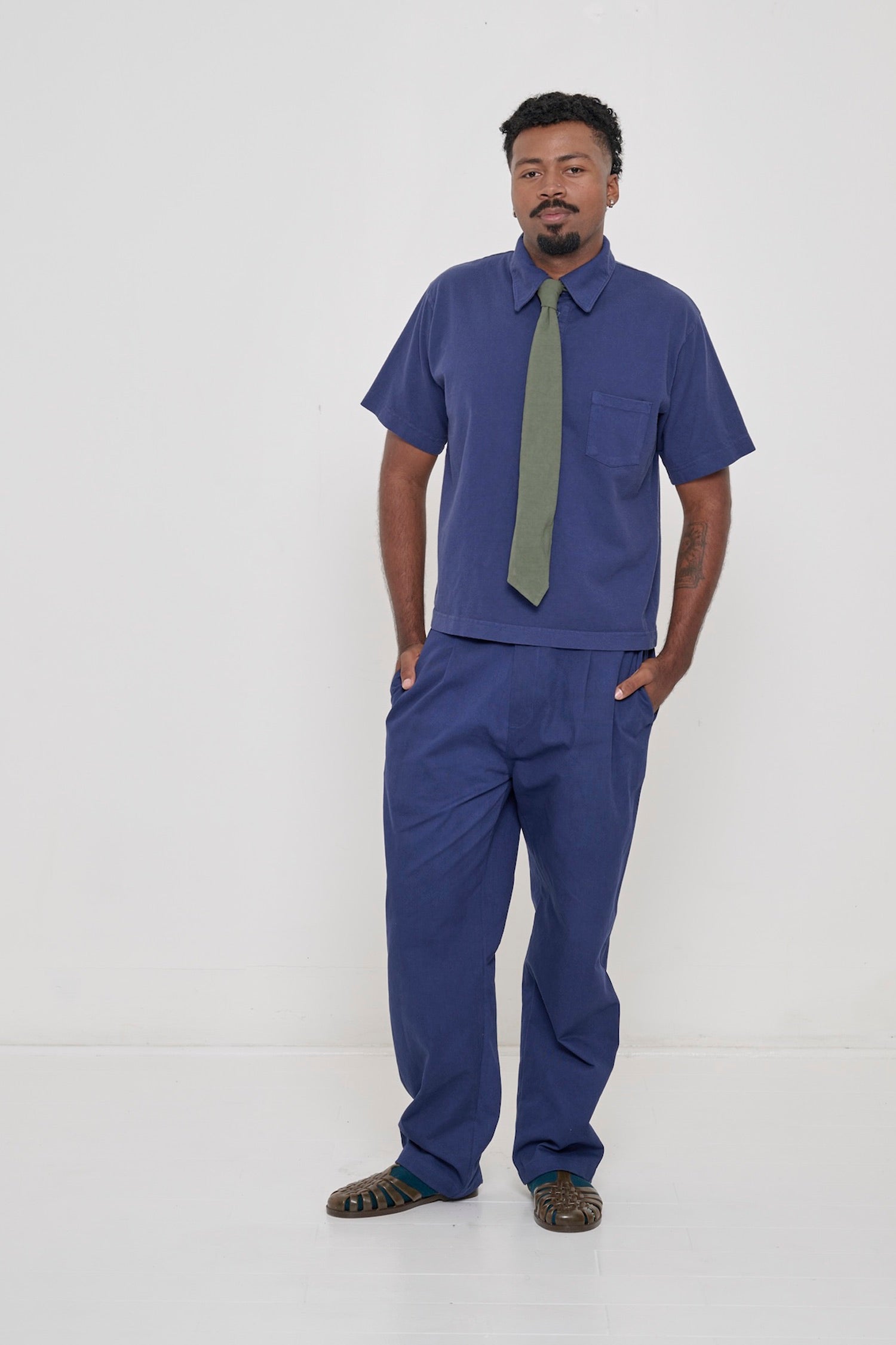 Full length profile view of a man wearing a Washed Navy Trash Polo with matching Life Uniform Pants and a Pine Trash Tie.