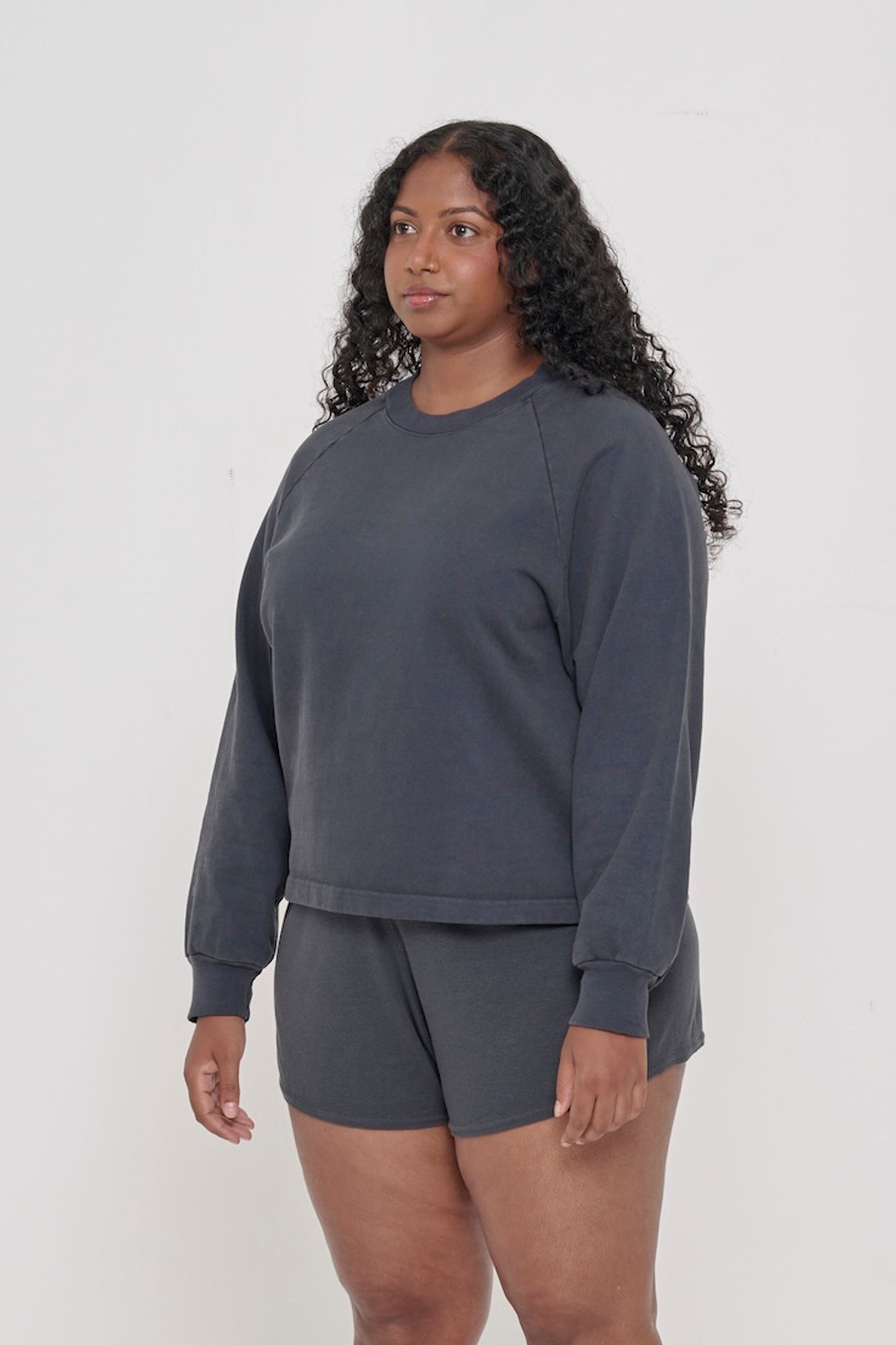 A woman facing 45-degrees from the front, wearing a Slate Trash Raglan, showcasing sleeve's relaxed fit.
