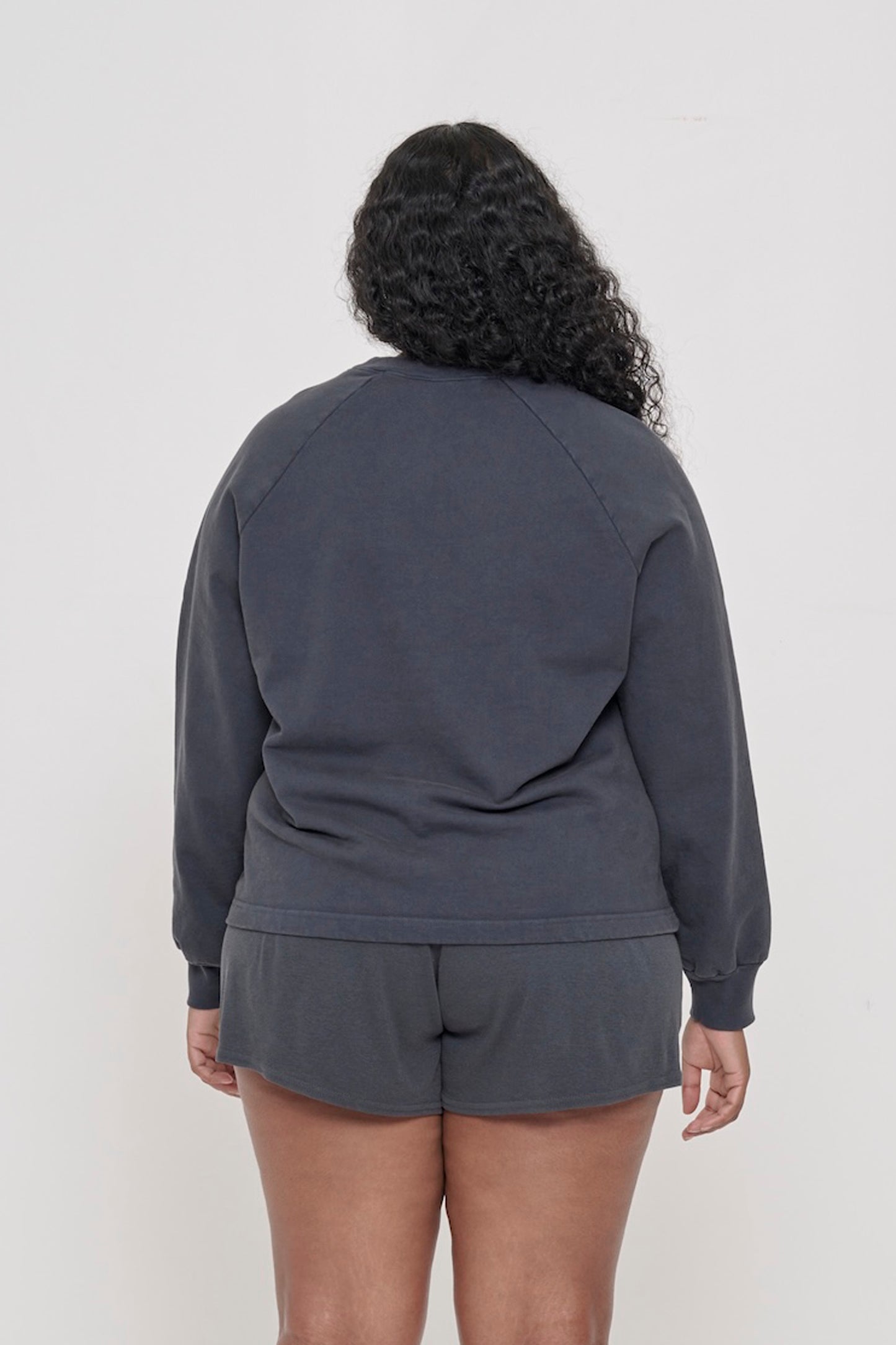 Slate Trash Crewneck, back view on a person. Relaxed throughout except for the rib cuffs.