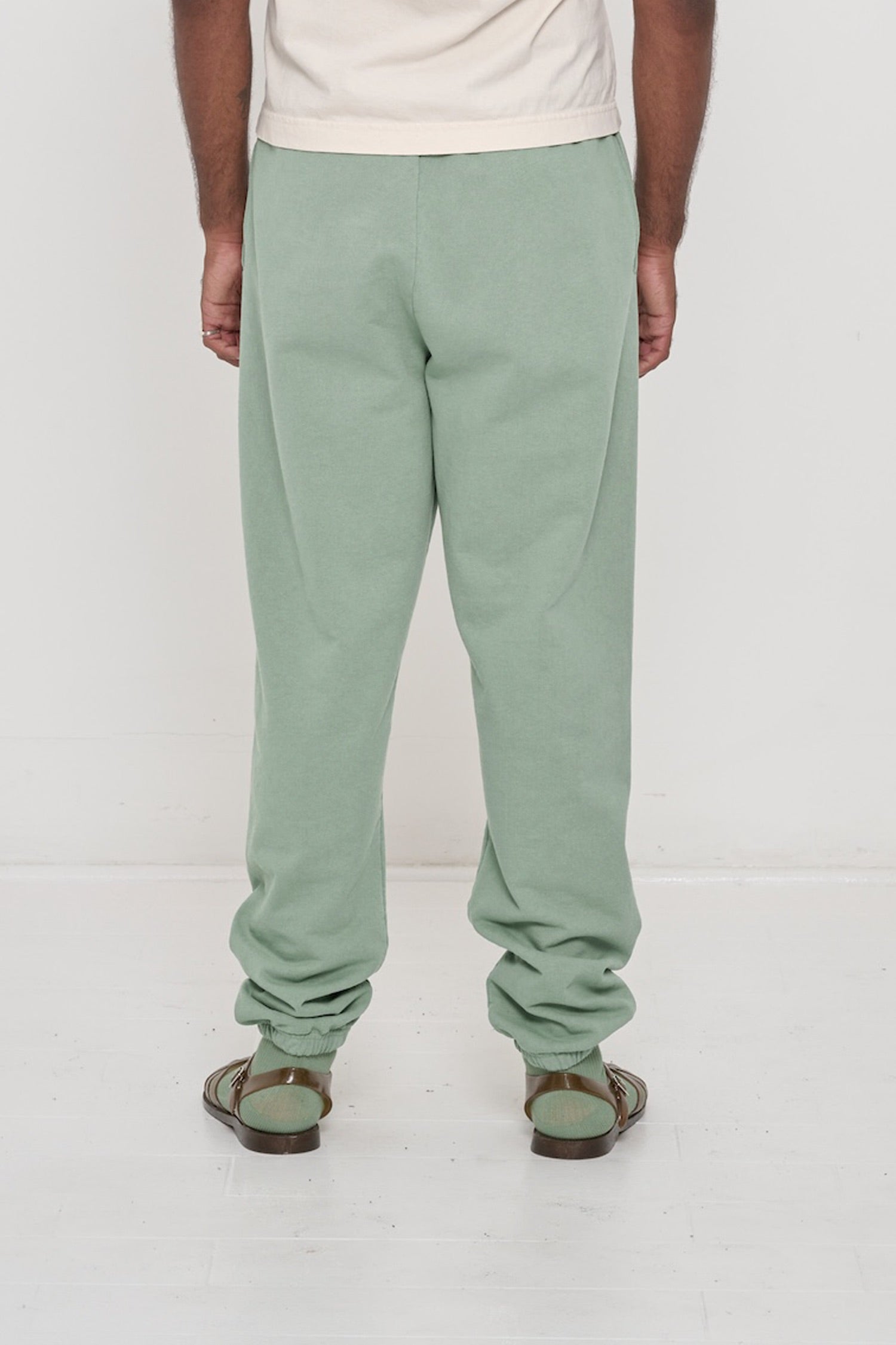 Back view of a person wearing Wasabi Trash Sweatpants, relaxed fit throughout, except for elastic waistband and cuffs.