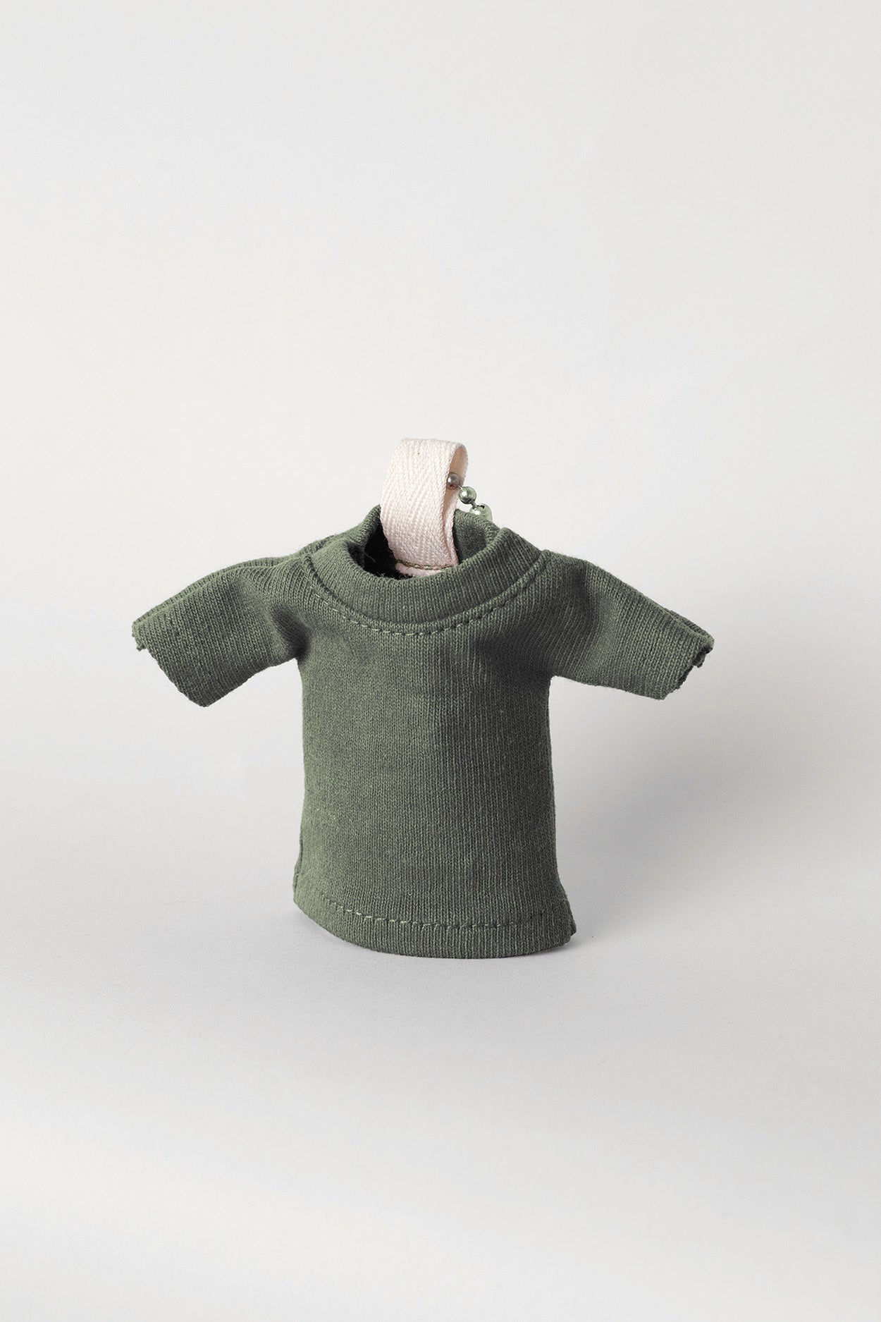 Pine T-shirt keychain, propped up, against a light gray background