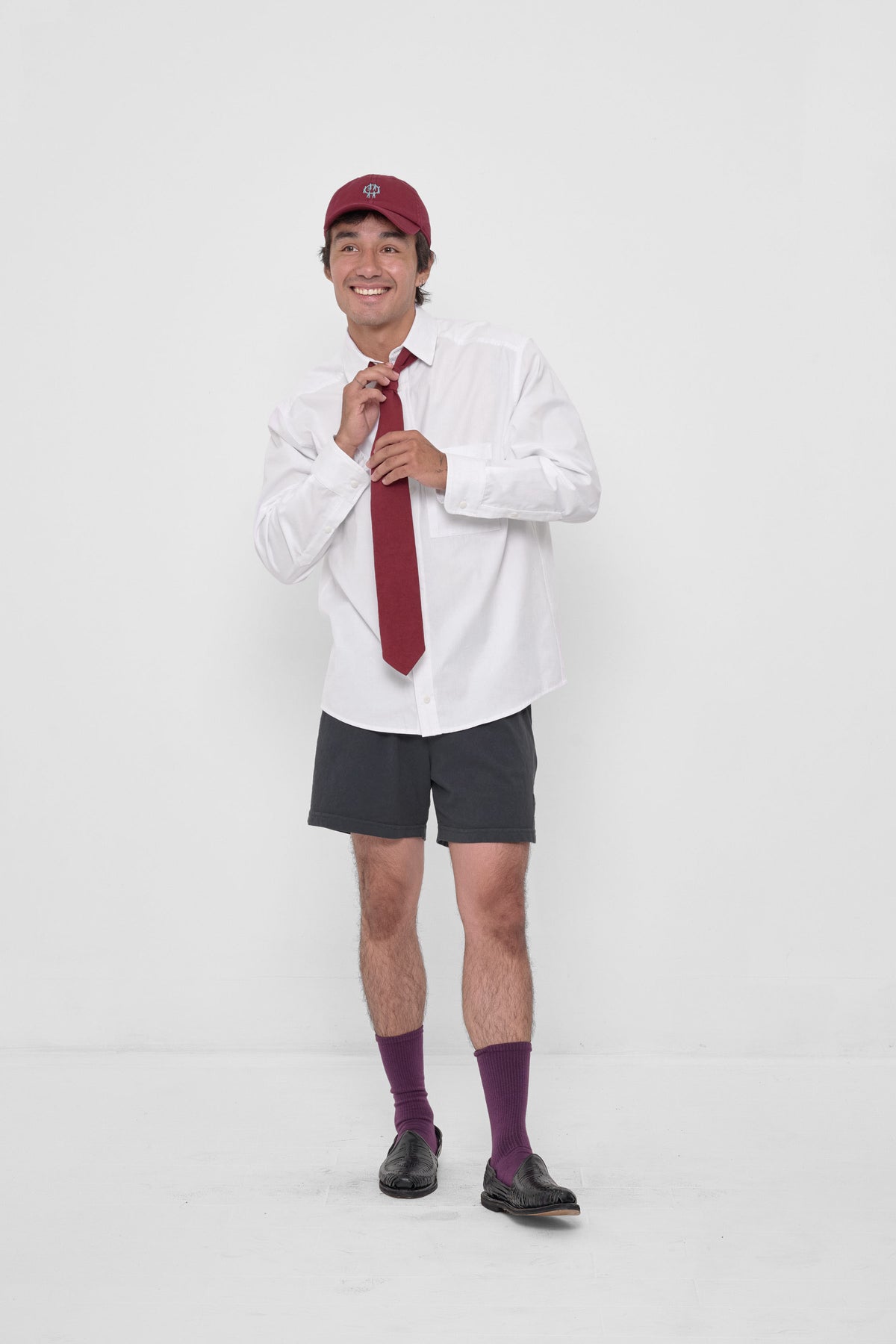 Trash Tie in Garnet – on a model, styled with a White Peach Fuzz Button-Up Shirt, Slate Everyday Shorts, and Garnet Bucky Logo Cap